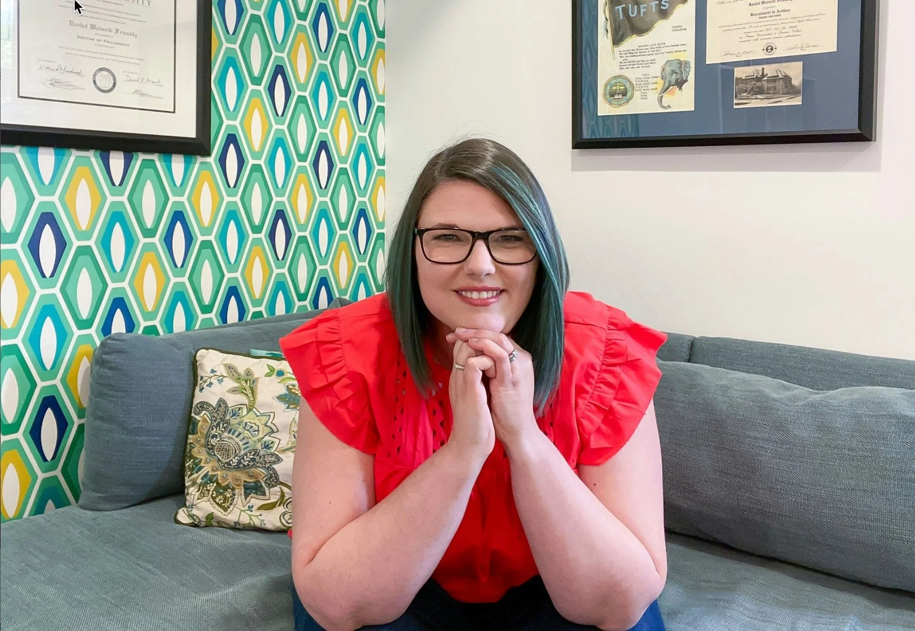 Rachel W. Friendly, Ph.D. is a therapist in Fairfax, VA sitting on a blue couch, wearing an orange top and jeans with glasses.