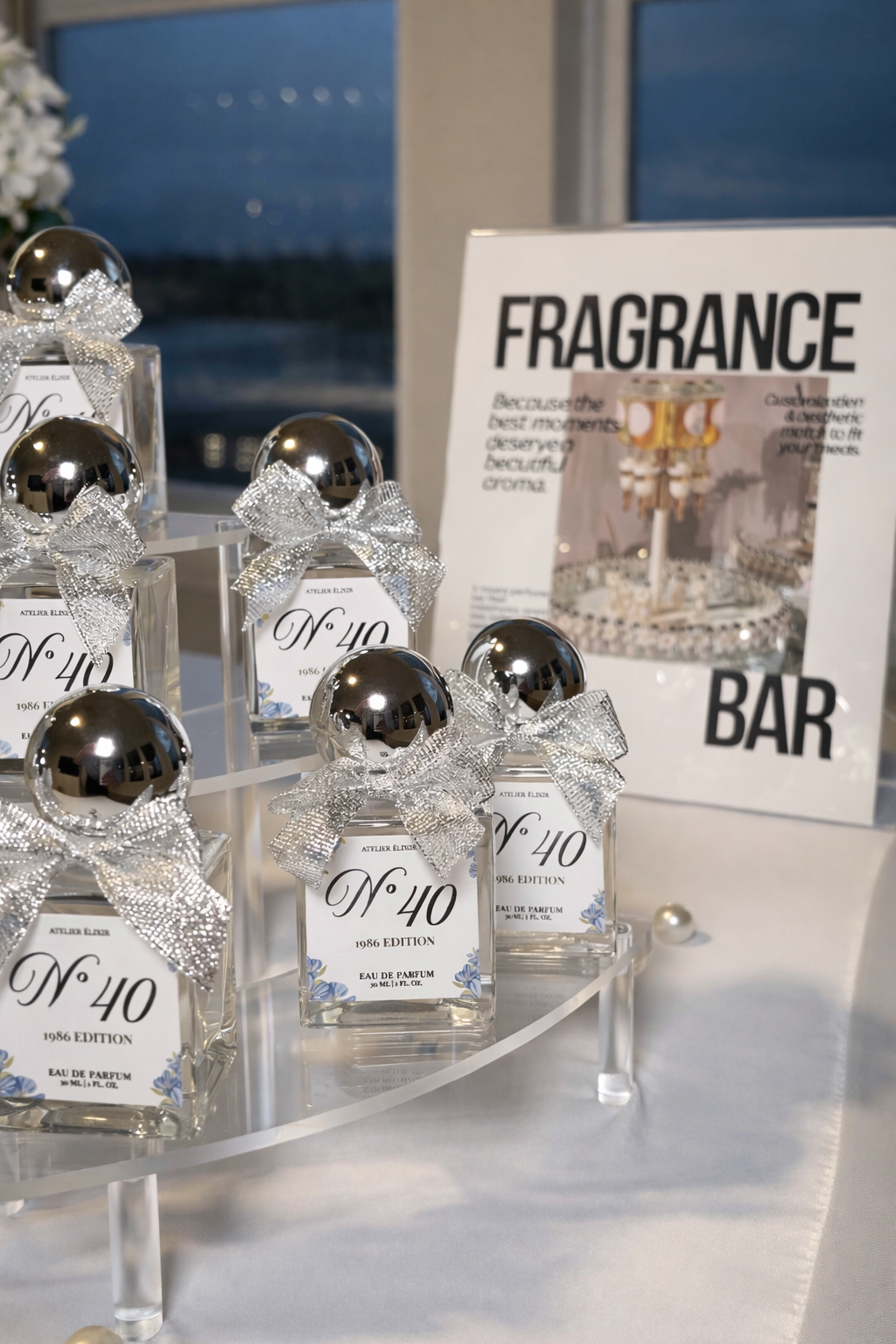 Display of perfume bottles with silver bows and black caps, labeled 'No. 40', arranged on a white stand. In the background, a sign promoting a fragrance bar and a window with a scenic view.