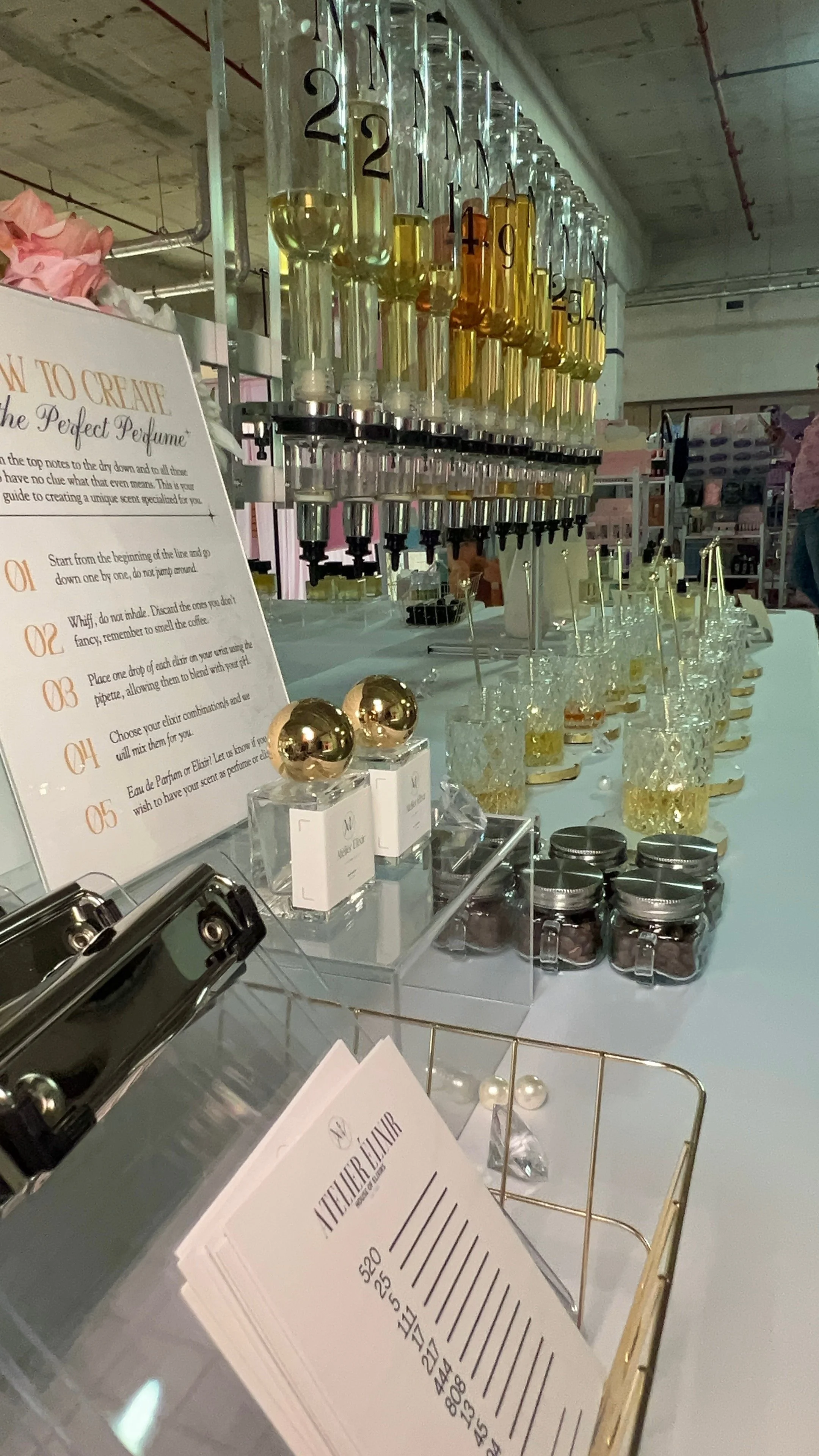 A perfume atelier display with perfume bottles and scent creation instructions, including a chart with numbered steps, glass jars with small chocolates, and a sample booklet for perfume mixing.