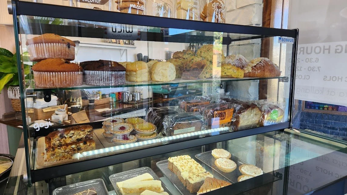 Display case with various baked goods, including muffins, scones, cakes, tarts, and bread, in a bakery shop.