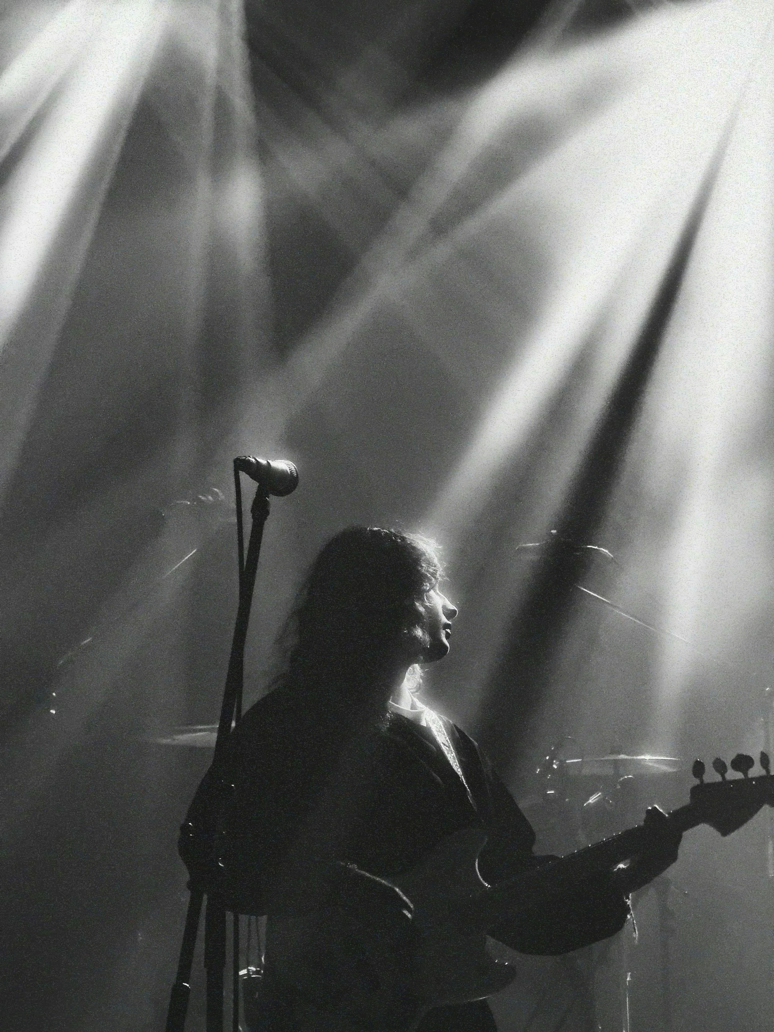 A person singing or speaking into a microphone on a stage, illuminated by light beams and surrounded by fog or smoke.