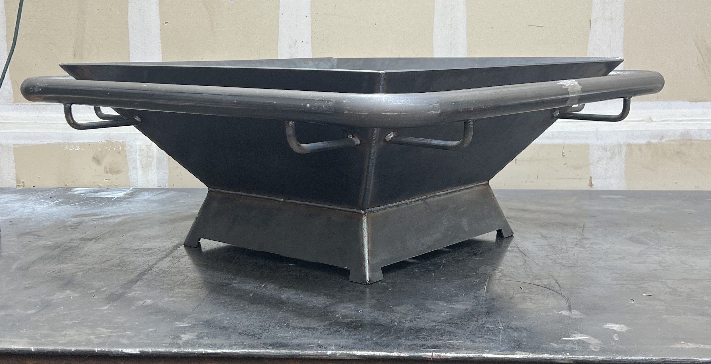 Built for homeowners and outdoor living spaces across Dallas–Fort Worth, this custom square steel fire pit features a deep tapered bowl, heavy-duty pedestal base, and a wraparound tubular safety rail for both style and function. Its durable black fin