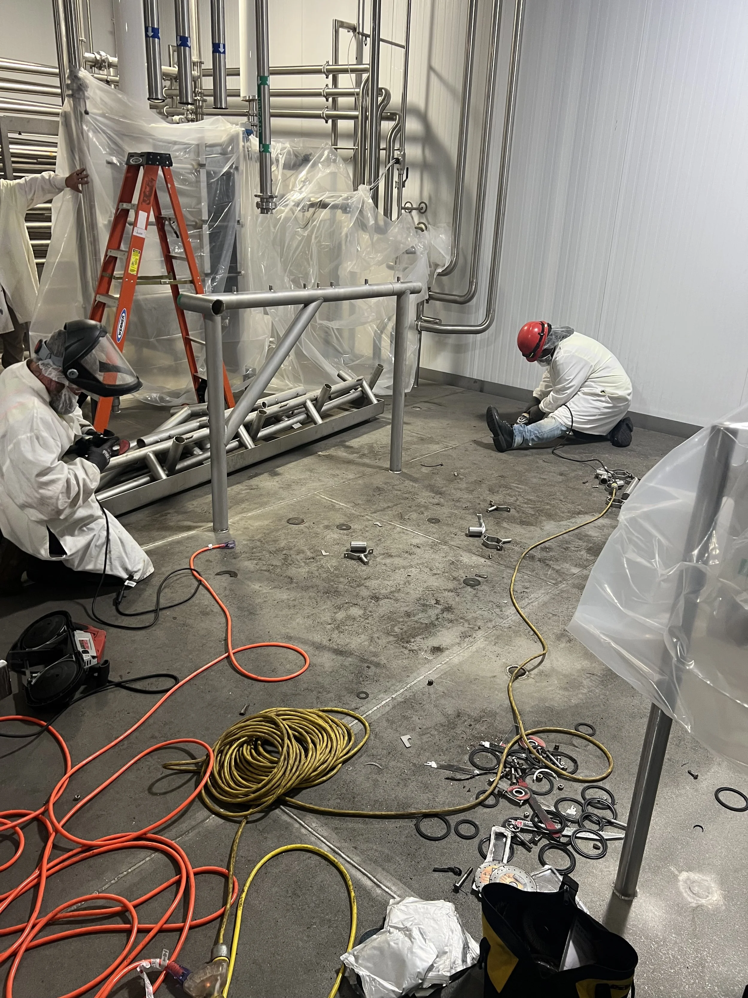 Midway progress on stainless steel demolition at a DFW food plant, with partially removed equipment and active dismantling in progress. Skilled contractors safely cutting and removing stainless steel tanks and piping in a food-grade facility