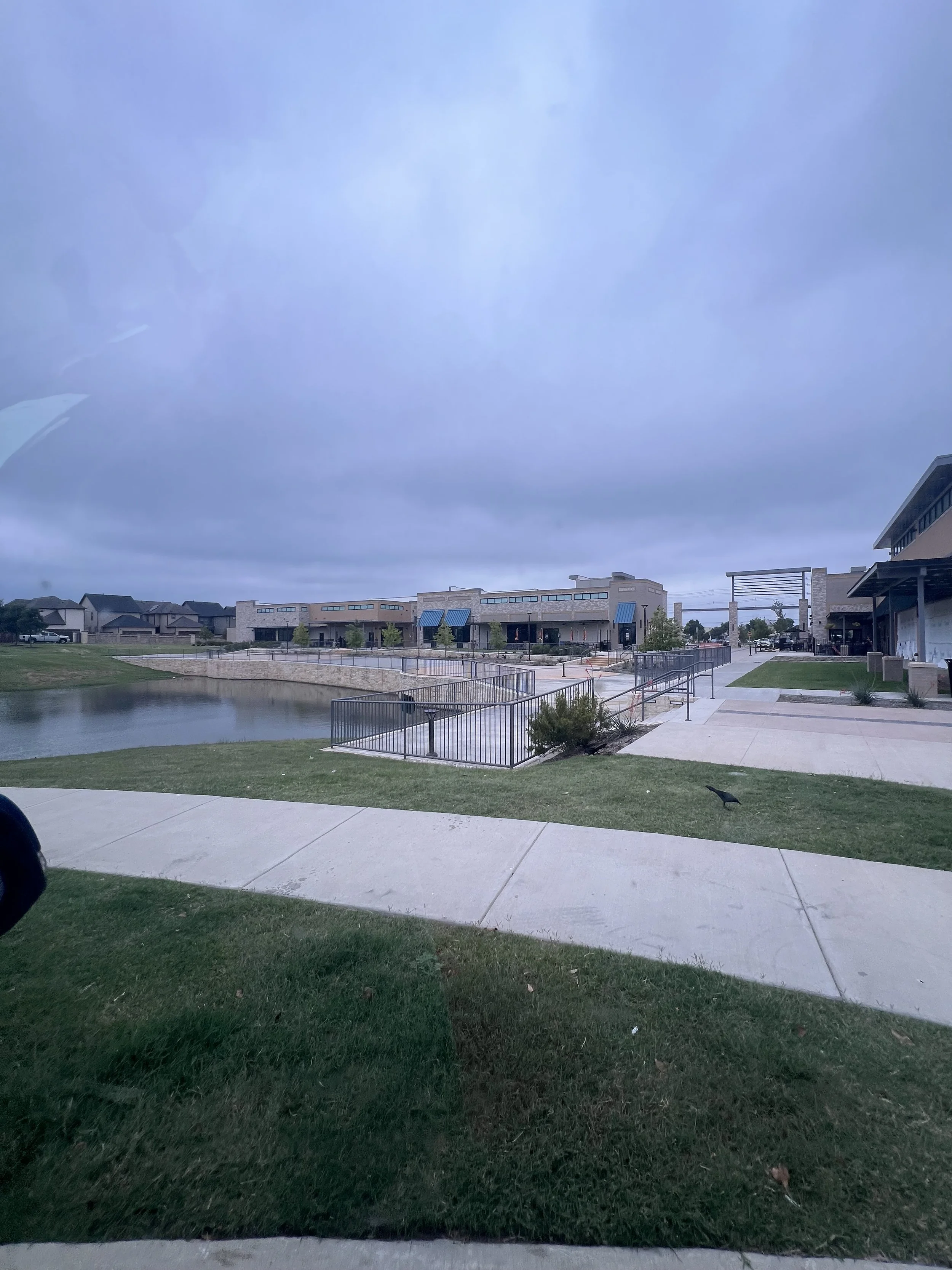 This project features a custom commercial metal railing installation at a shopping center in Frisco, Texas, designed to follow the natural curves of a pond-side walkway. The system includes integrated railings for stairs, ADA-compliant ramps, and ped