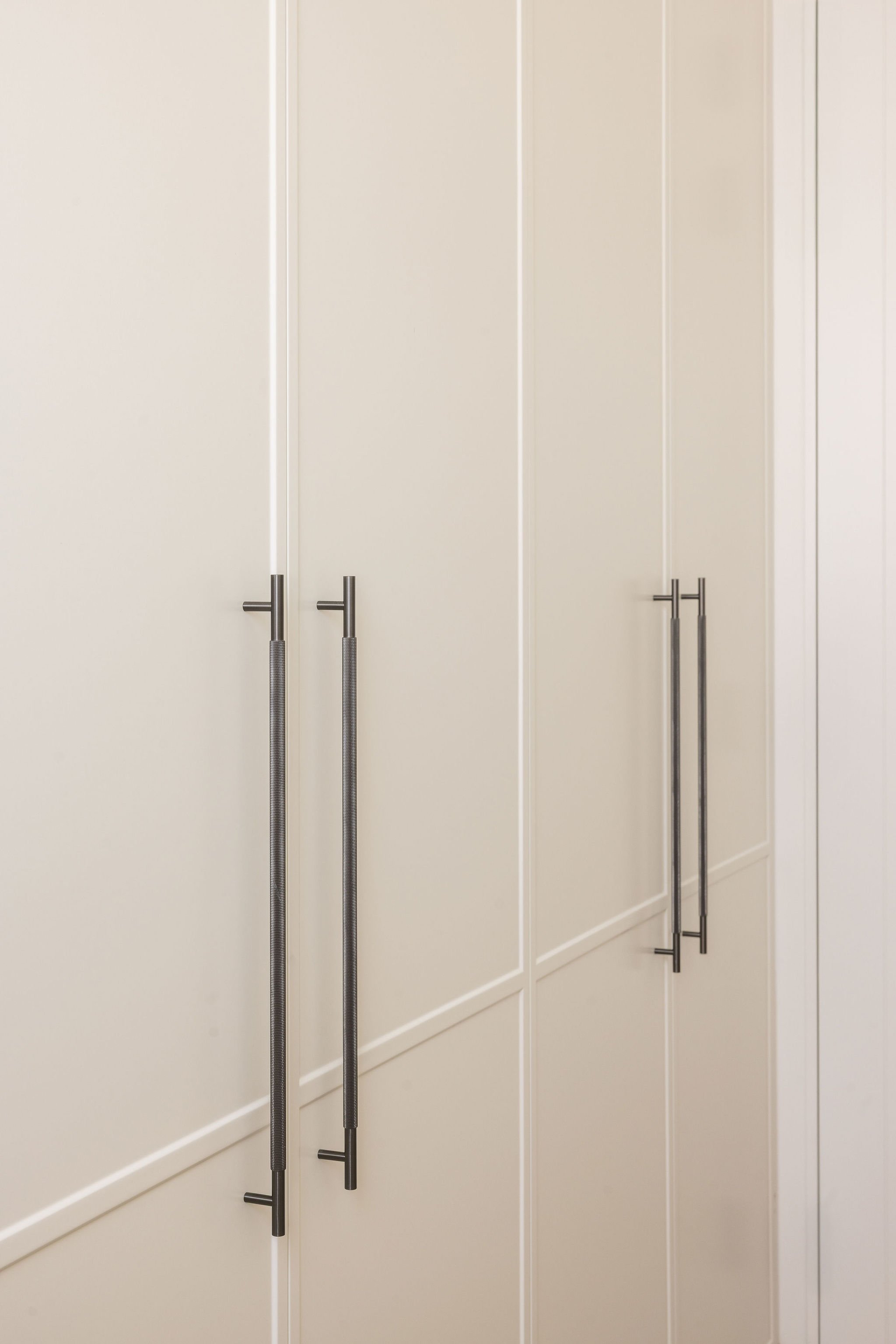 A wardrobe with four closed cream-colored doors and four long black handles, two on each door.