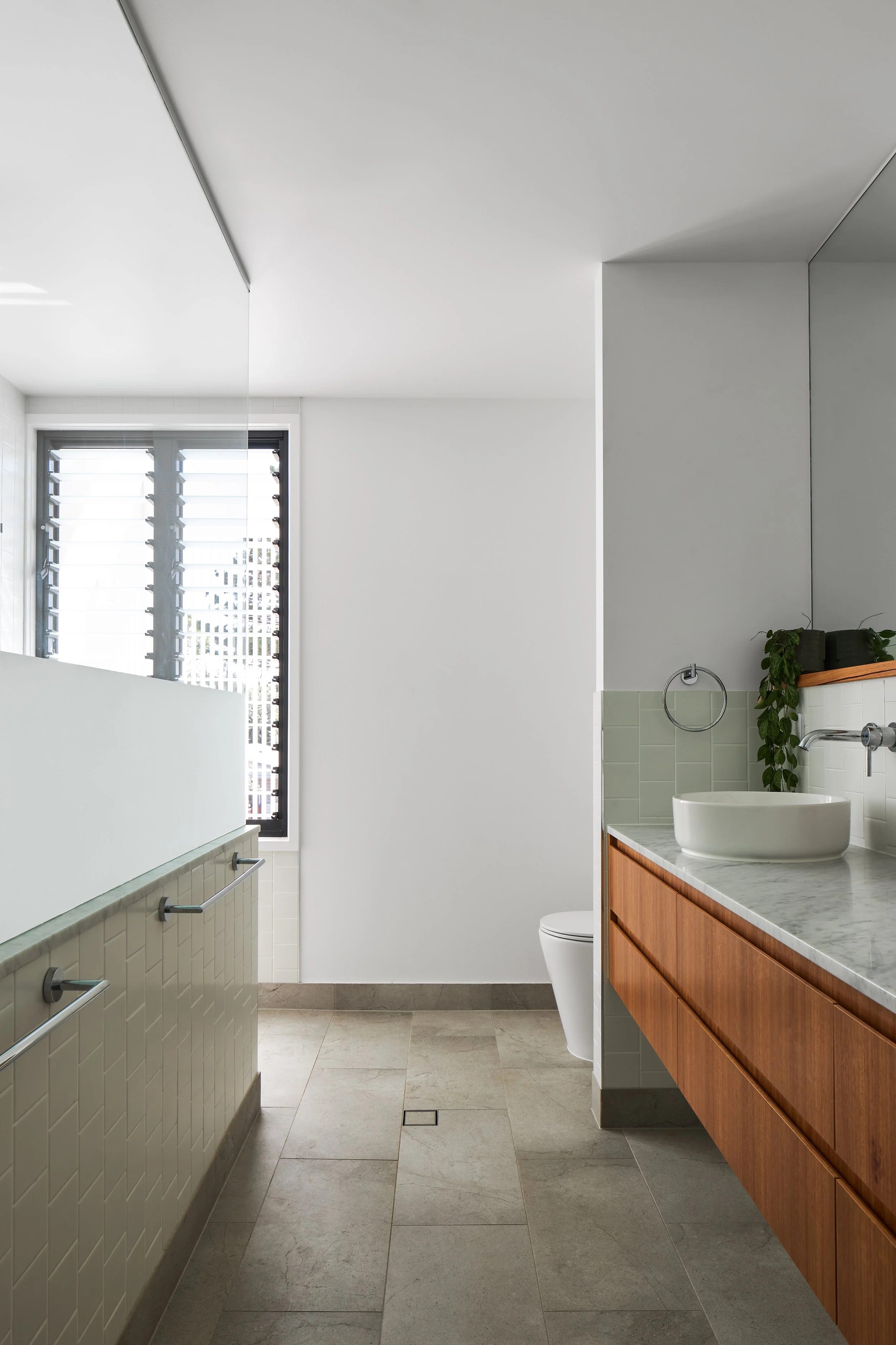 Modern bathroom with large window, white walls, beige tile floor, wooden vanity with stone countertop, vessel sink, and a mirror.