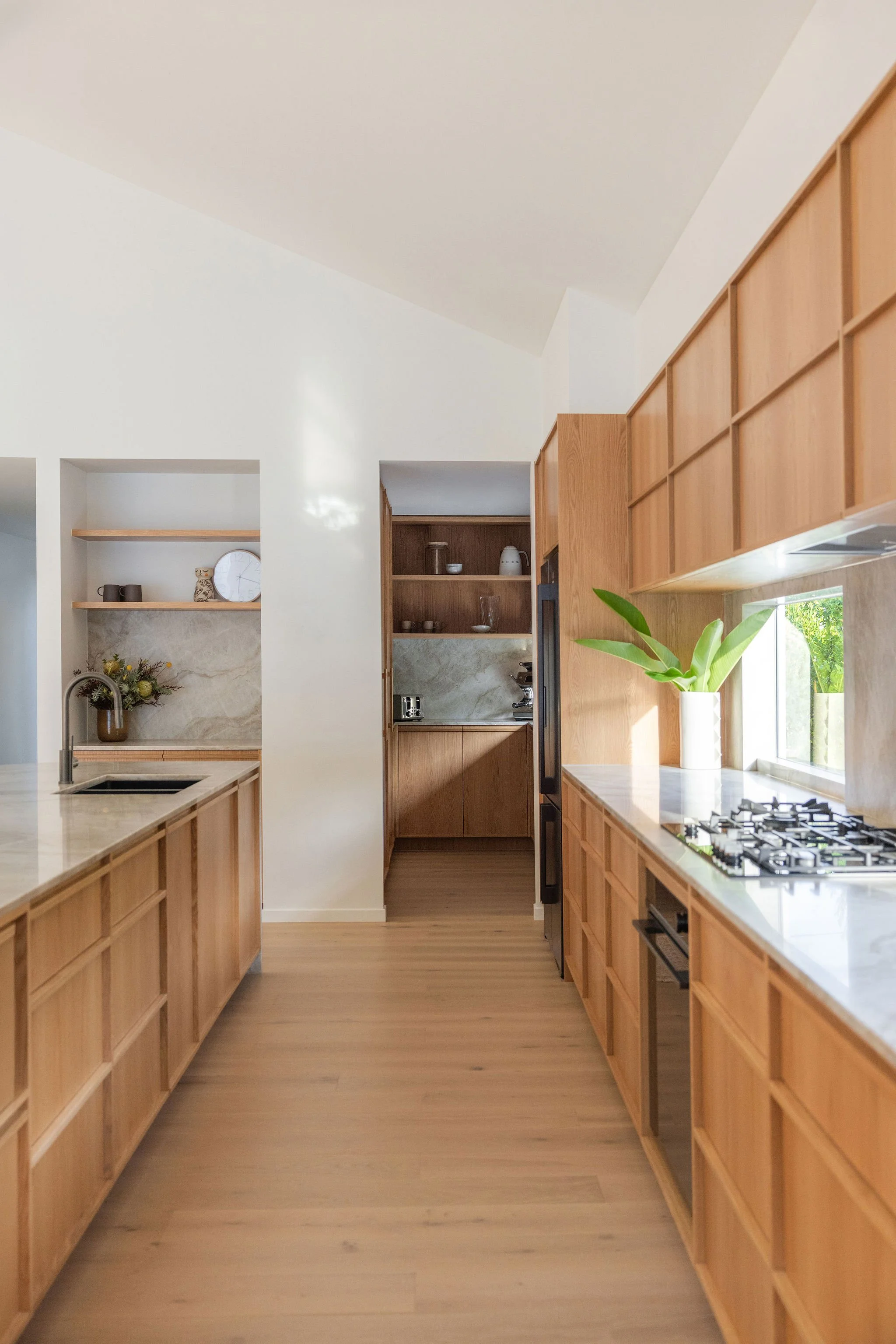 A modern kitchen with wooden cabinets, a marble backsplash, and a large window with greenery outside.