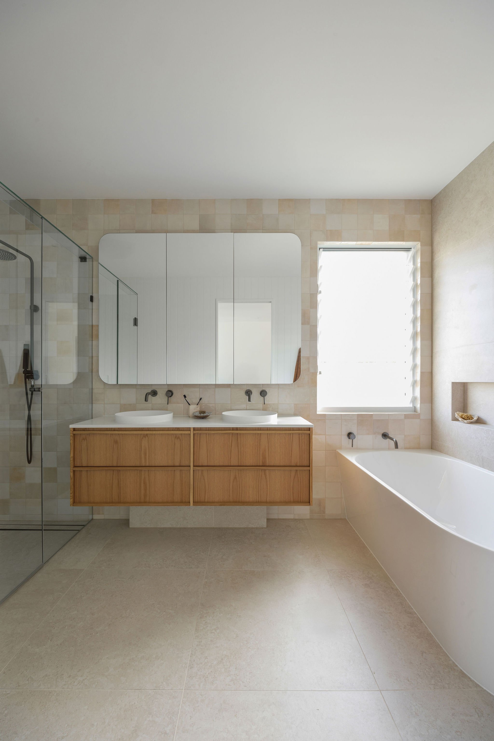 A modern bathroom with a double vanity with two vessel sinks, a large mirror, a bathtub, a window, and a shower with glass door.