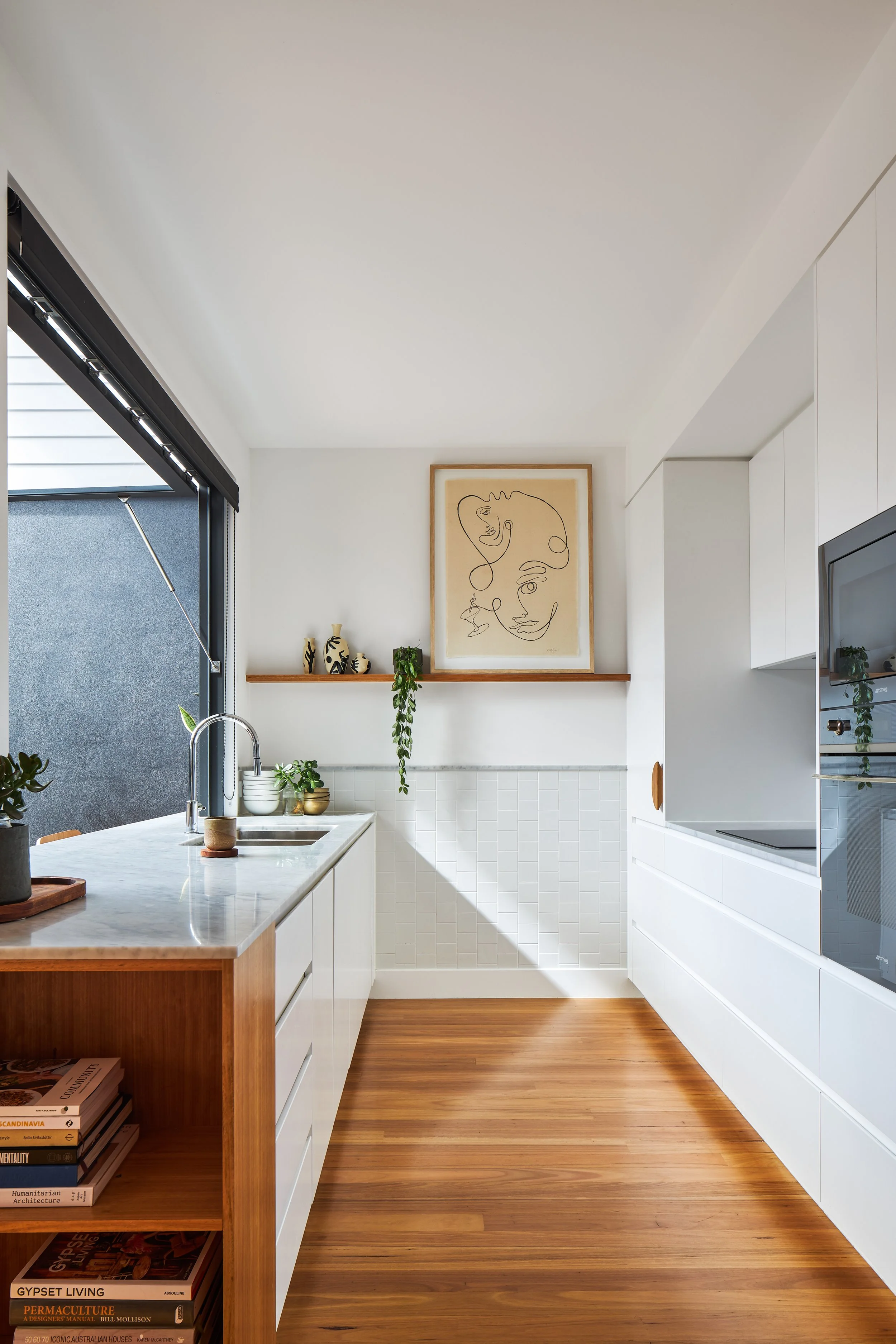 Modern kitchen with white cabinets, wooden countertop, plants, abstract line art painting, and wooden flooring.