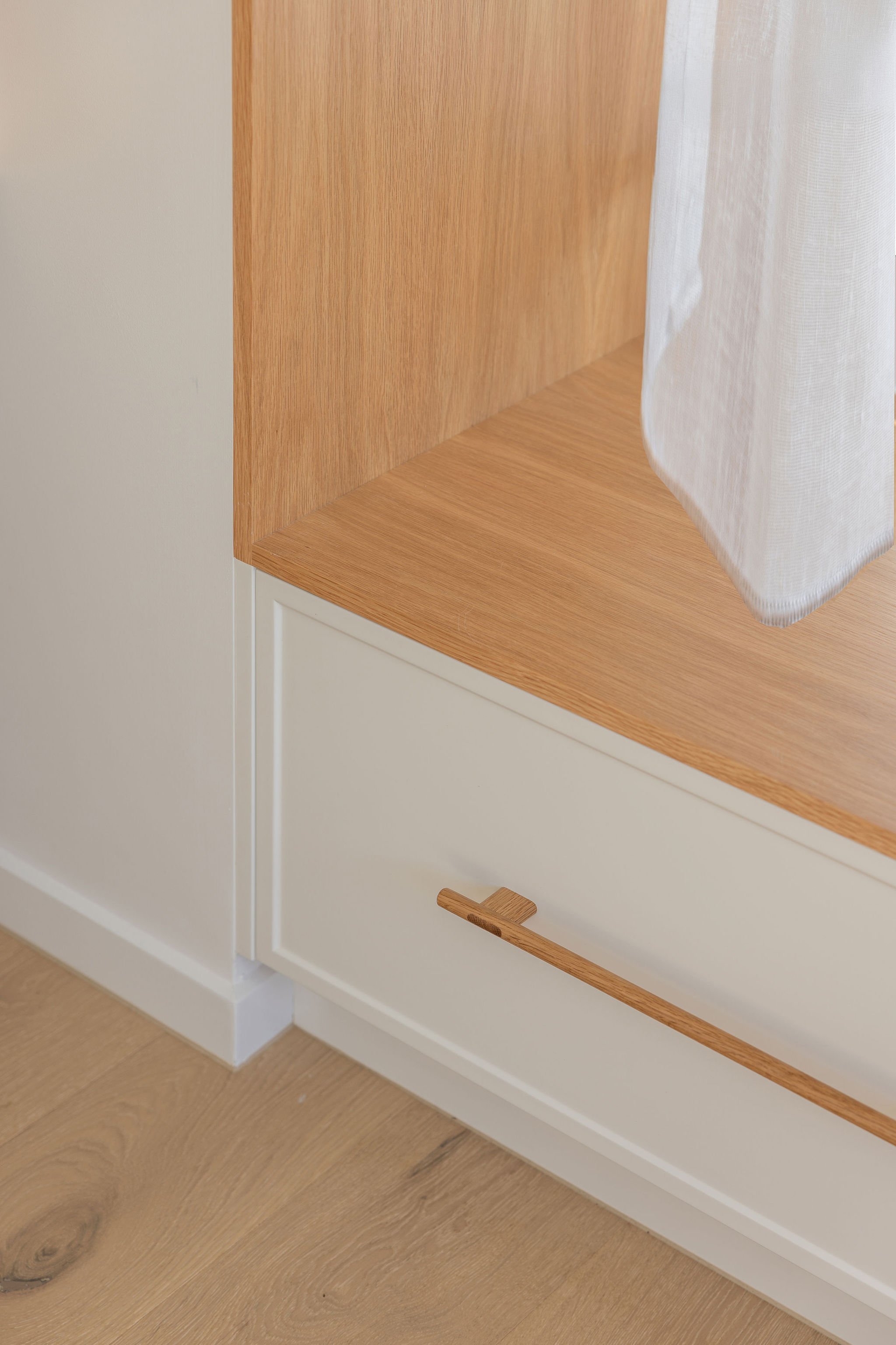 Close-up of a wooden cabinet with a drawer and a white curtain partially covering the right side.
