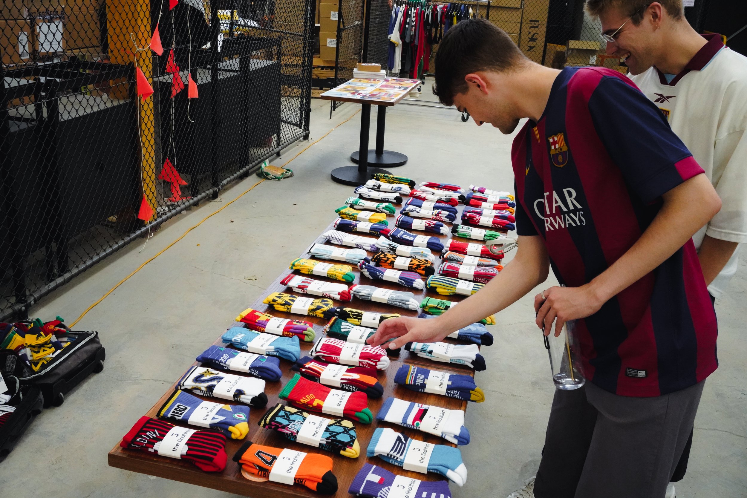 People browsing shelves of colorful socks at a merchandise stall in an indoor setting.