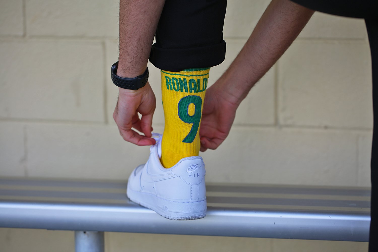 A person is putting on a white Nike Air sneaker while wearing a yellow sock with a green and blue design featuring the name 'Ronaldo' and the number 9. The person's hand is adjusting the sock.