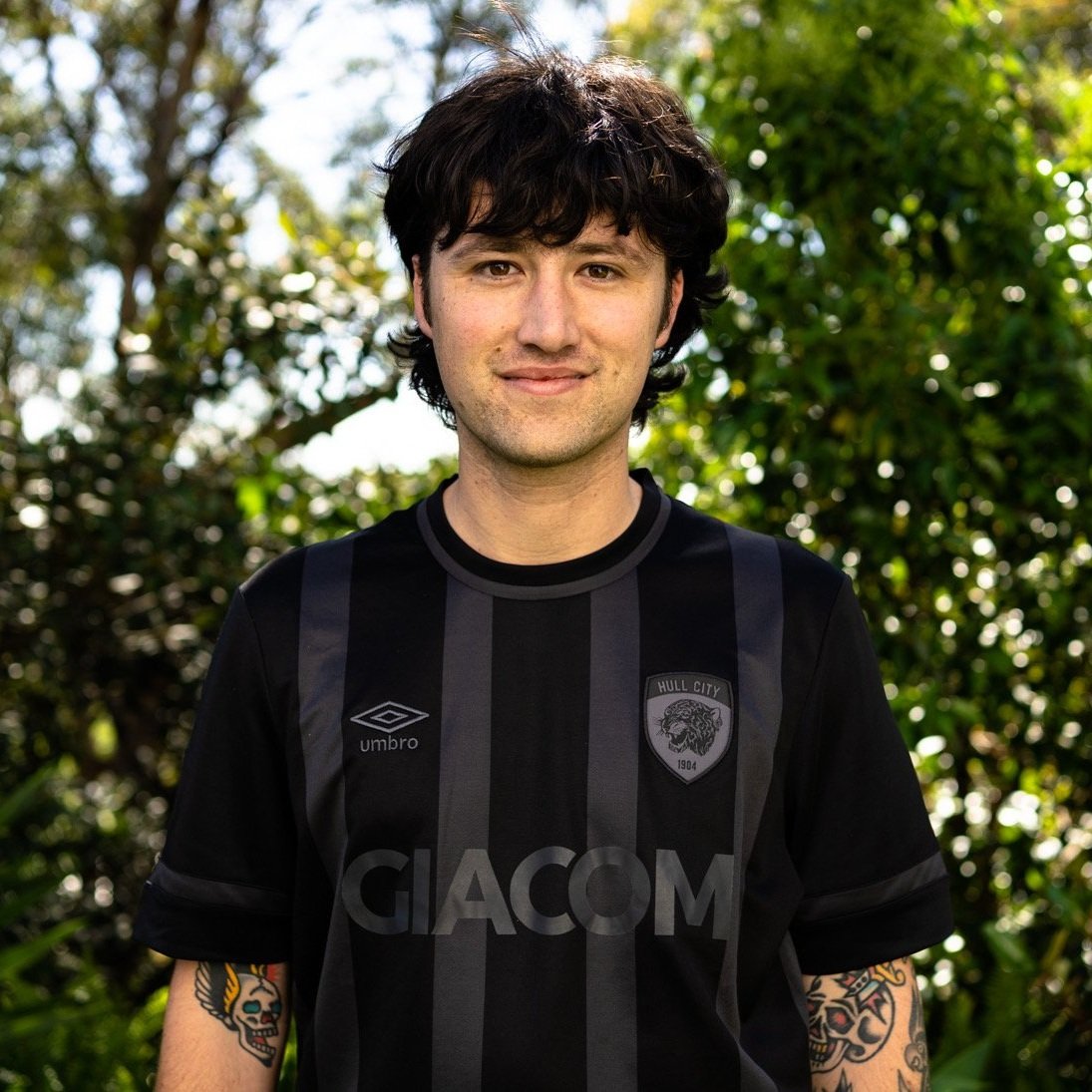 Young man with dark wavy hair, wearing a black and gray football jersey with a
