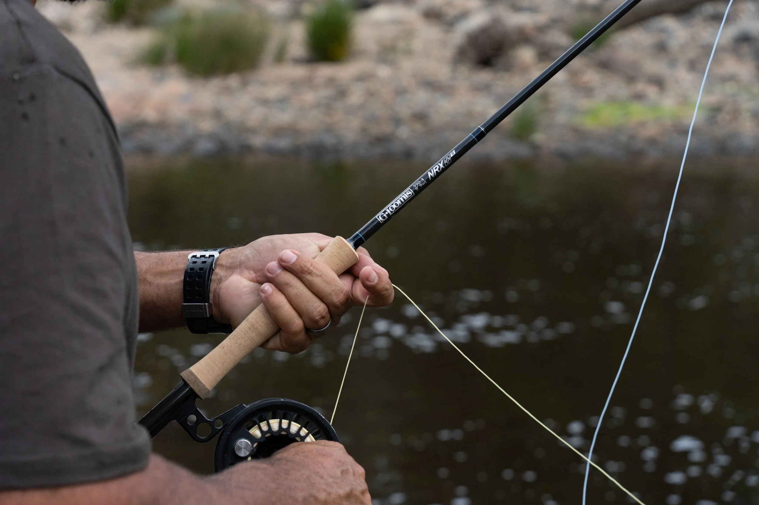 Close-up of a person holding a fishing rod near a body of water, with the fishing line cast into the water.