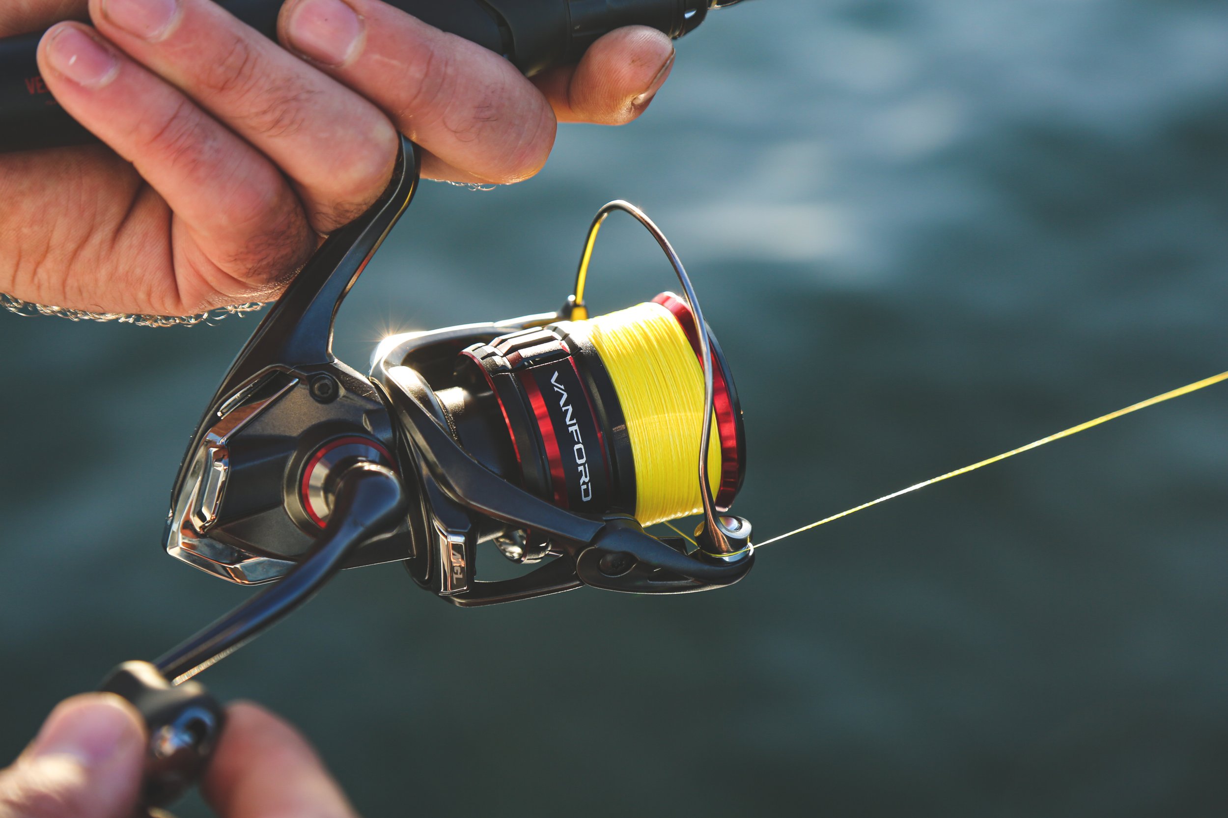 A person holding a fishing rod with a yellow fishing line extended over water.