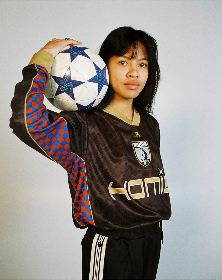 A woman in a soccer jersey holding a soccer ball on her shoulder.