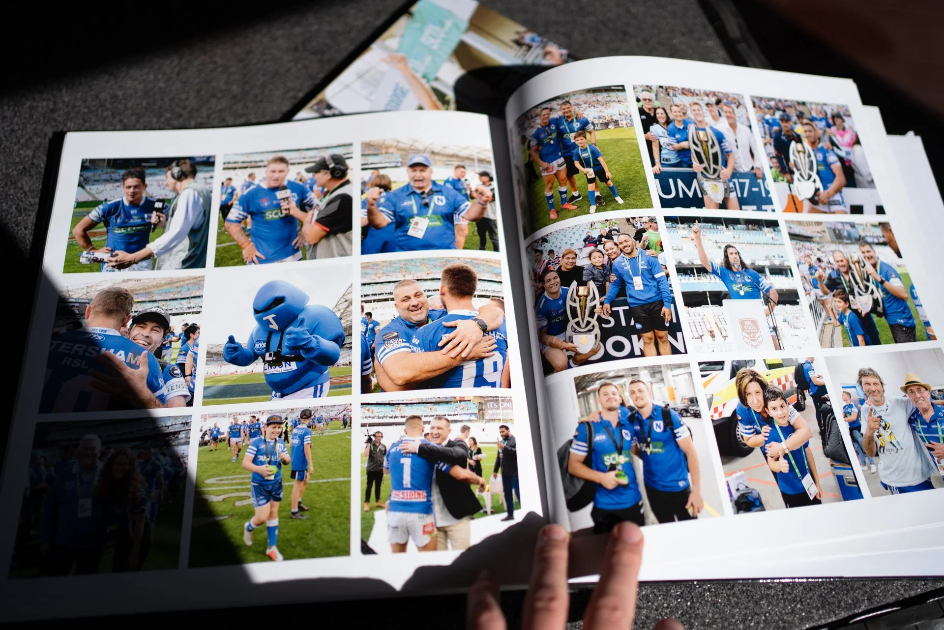 Open photo album featuring multiple images of athletes and fans at a sports event, with people in blue uniforms celebrating, hugging, and posing with trophies on a sports field.