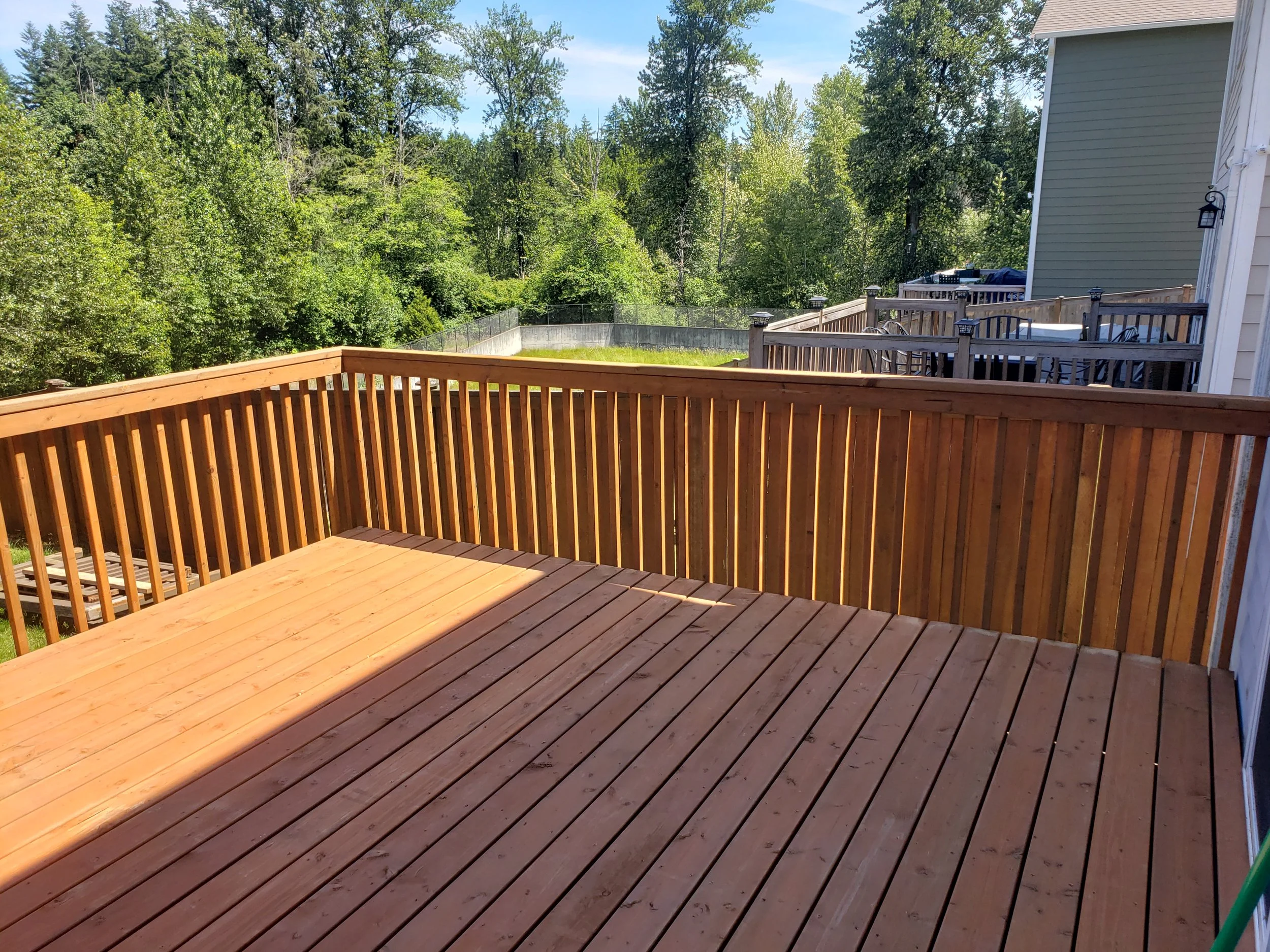 Wooden deck with railing overlooking a backyard with trees and neighboring houses.