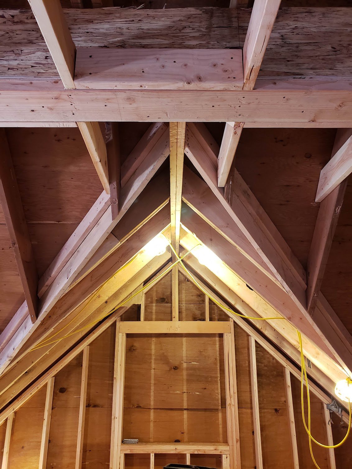 Interior view of an attic under construction, showing wooden framing and roof trusses.