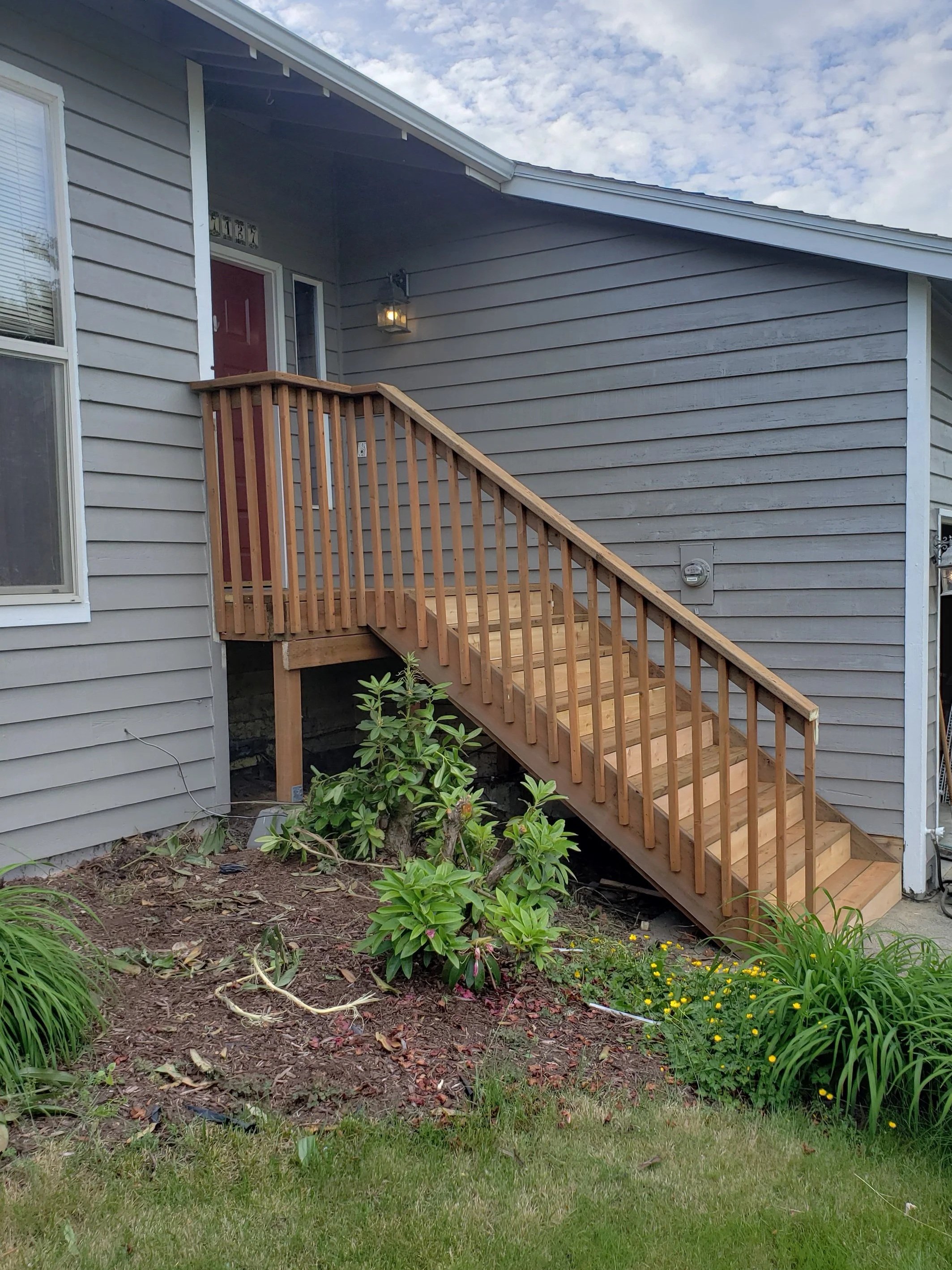Newly rebuilt front porch wooden staircase with railing.