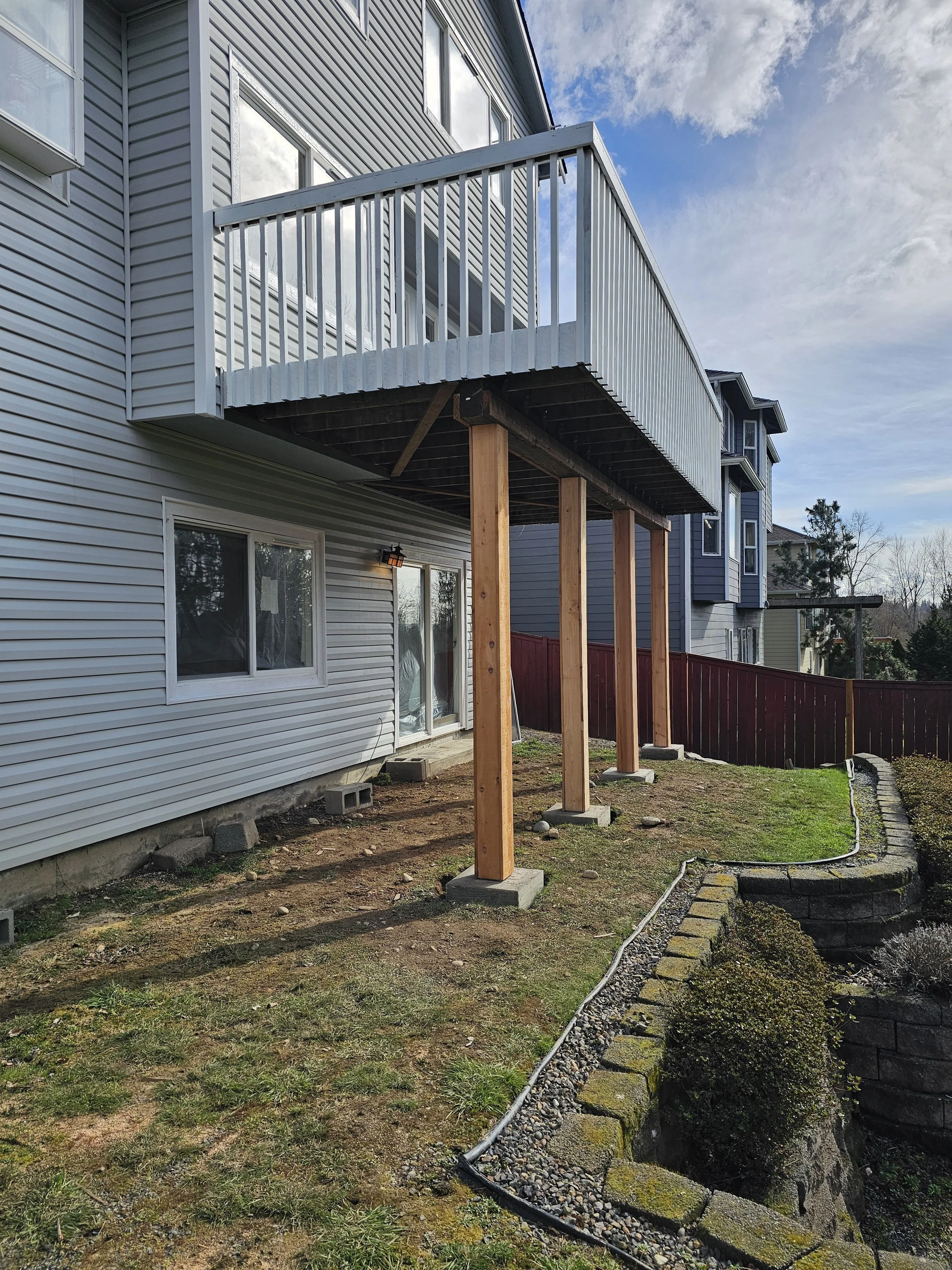 Back of a house with a newly built elevated balcony supported by wooden posts and concrete footings.