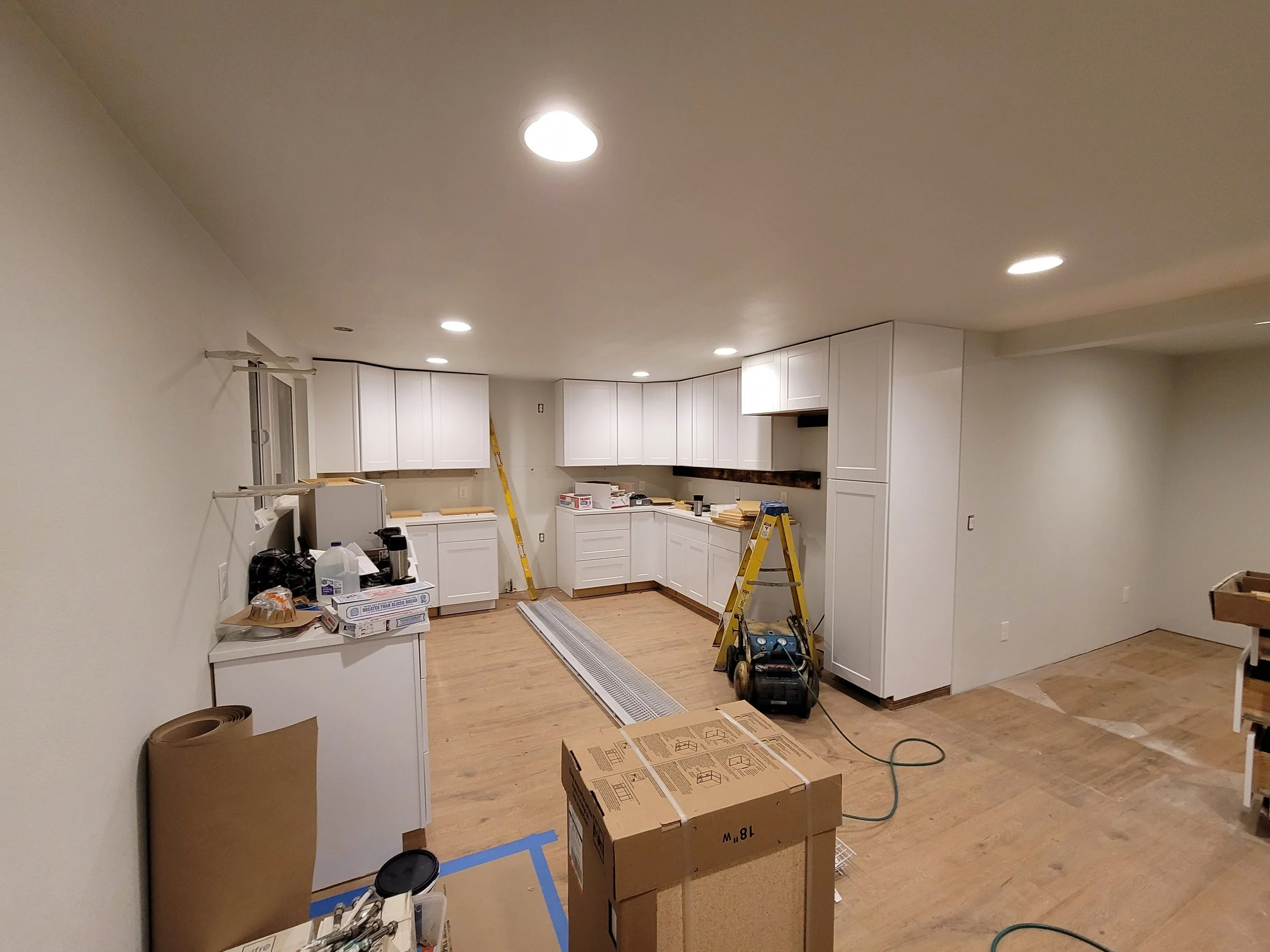 A remodel kitchen under construction with white cabinets, wooden flooring.