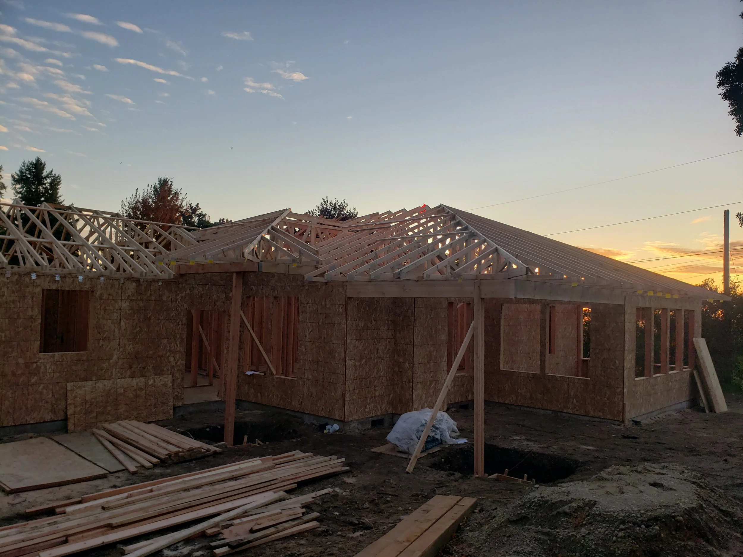 Construction site of a house during sunset, with wooden framing on the roof.