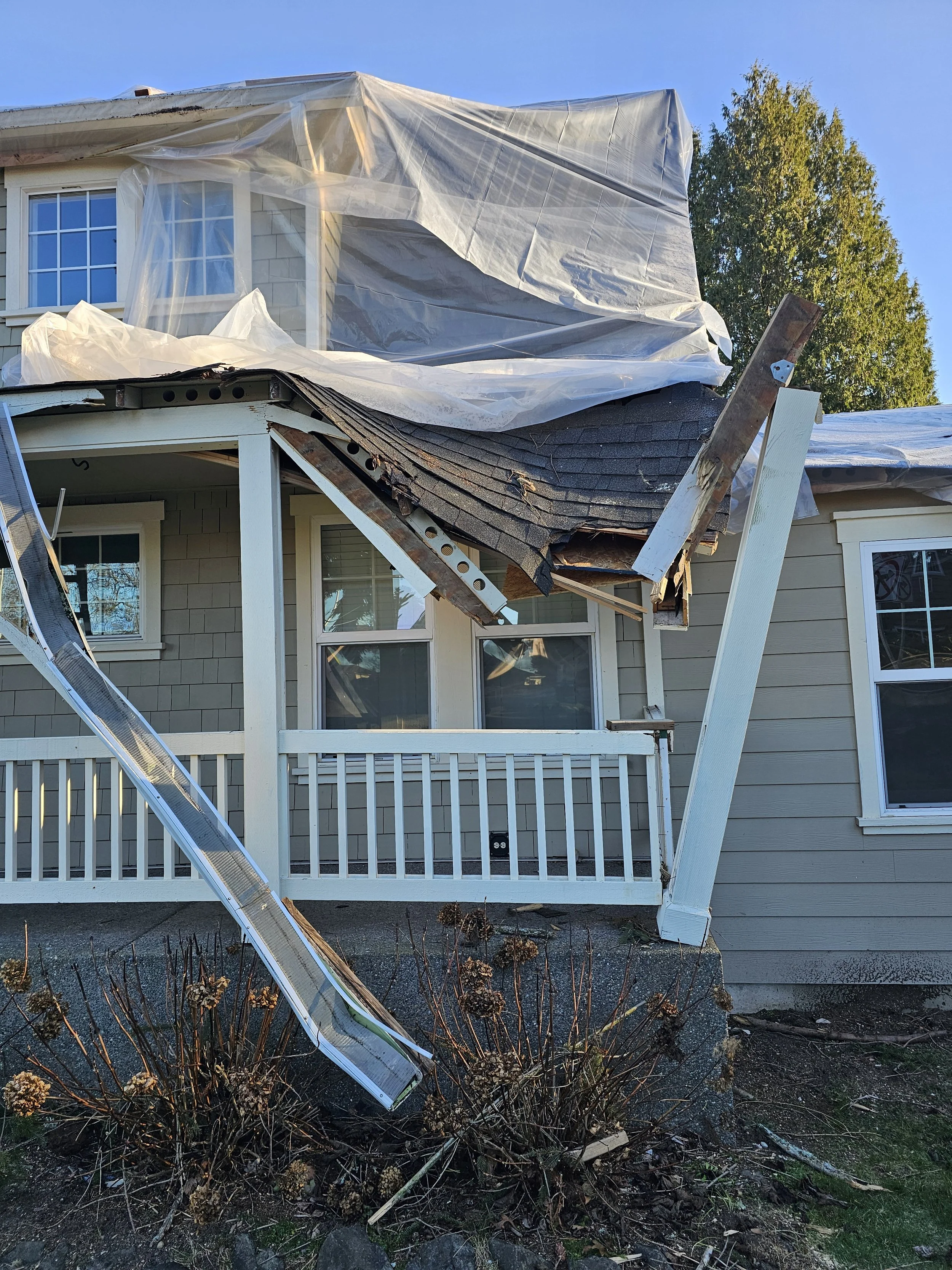 House with damage to the roof and exterior, debris, a ladder, and a tarp covering part of the house, indicating repair aftermath from a storm or accident.