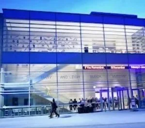 Exterior view of a modern airport terminal with glass facade, entrance doors, and people walking outside.