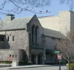 An old stone church with gothic windows and a small entrance, situated on a street with traffic signs, under a clear blue sky.