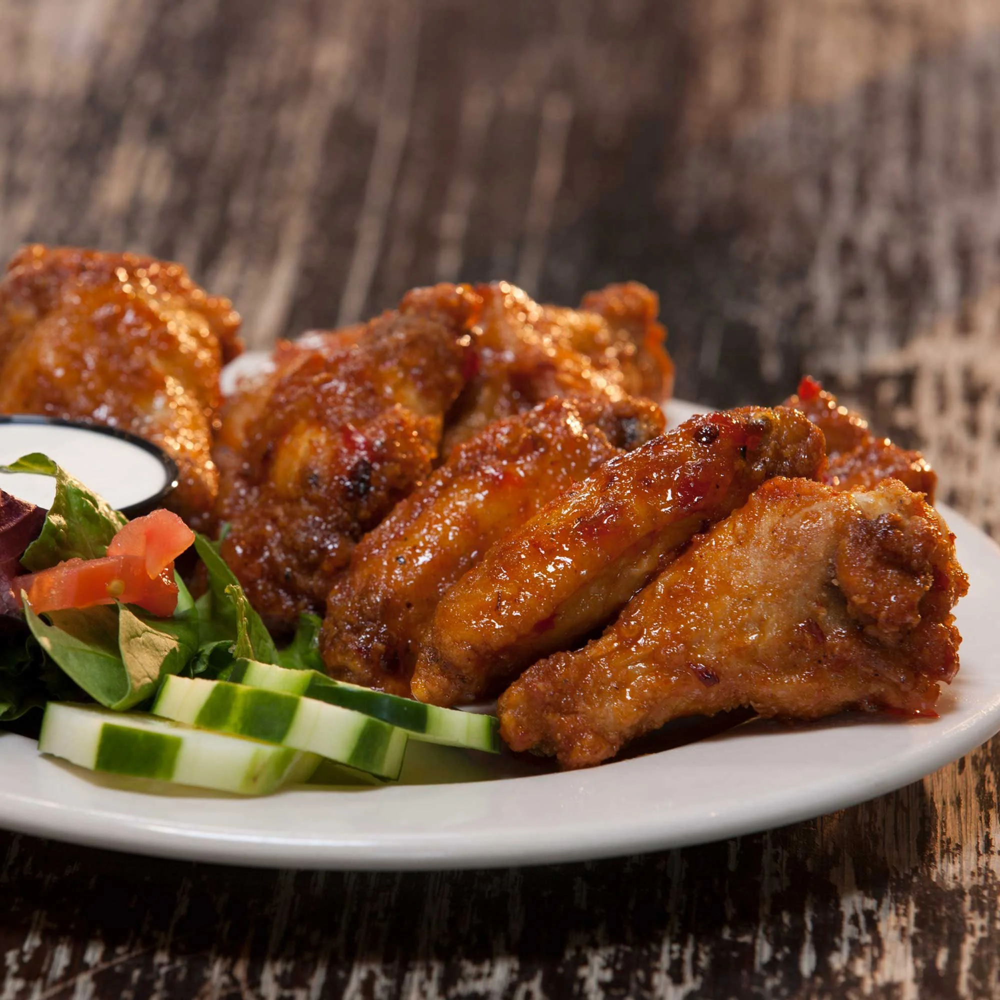 Plate of buffalo chicken wings with cucumber slices and salad leaves.