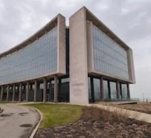 Modern office building with glass windows and a unique angular design, located near a curved road with grassy areas.