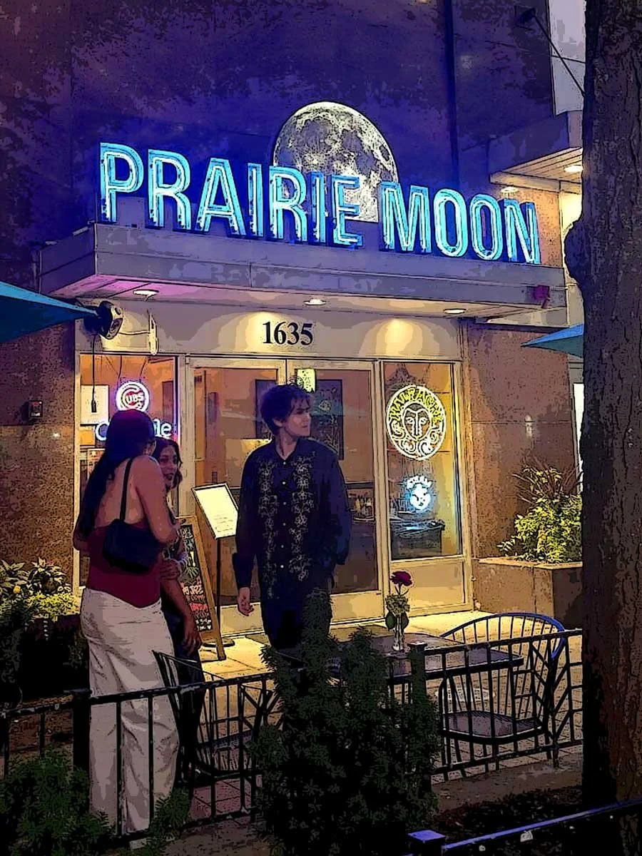A group of people standing outside a restaurant named Prairie Moon at night, with neon signs and a full moon graphic above the entrance.