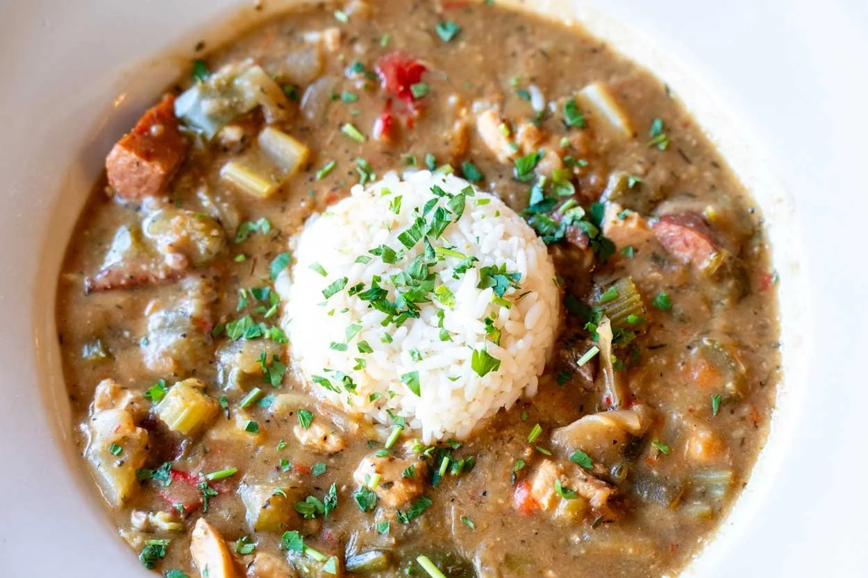 A bowl of hearty vegetable and chicken stew with rice, garnished with chopped parsley.
