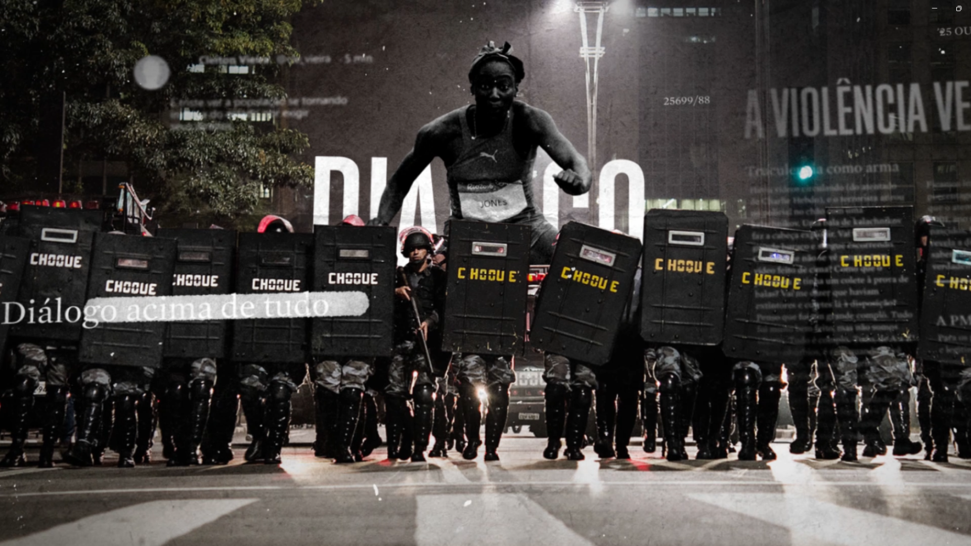 Manifestação com policiais de uniforme e escudos na rua durante a noite, com um grande painel de protesto ao fundo, exibindo a palavra 'Diálogo acima de tudo' em destaque.