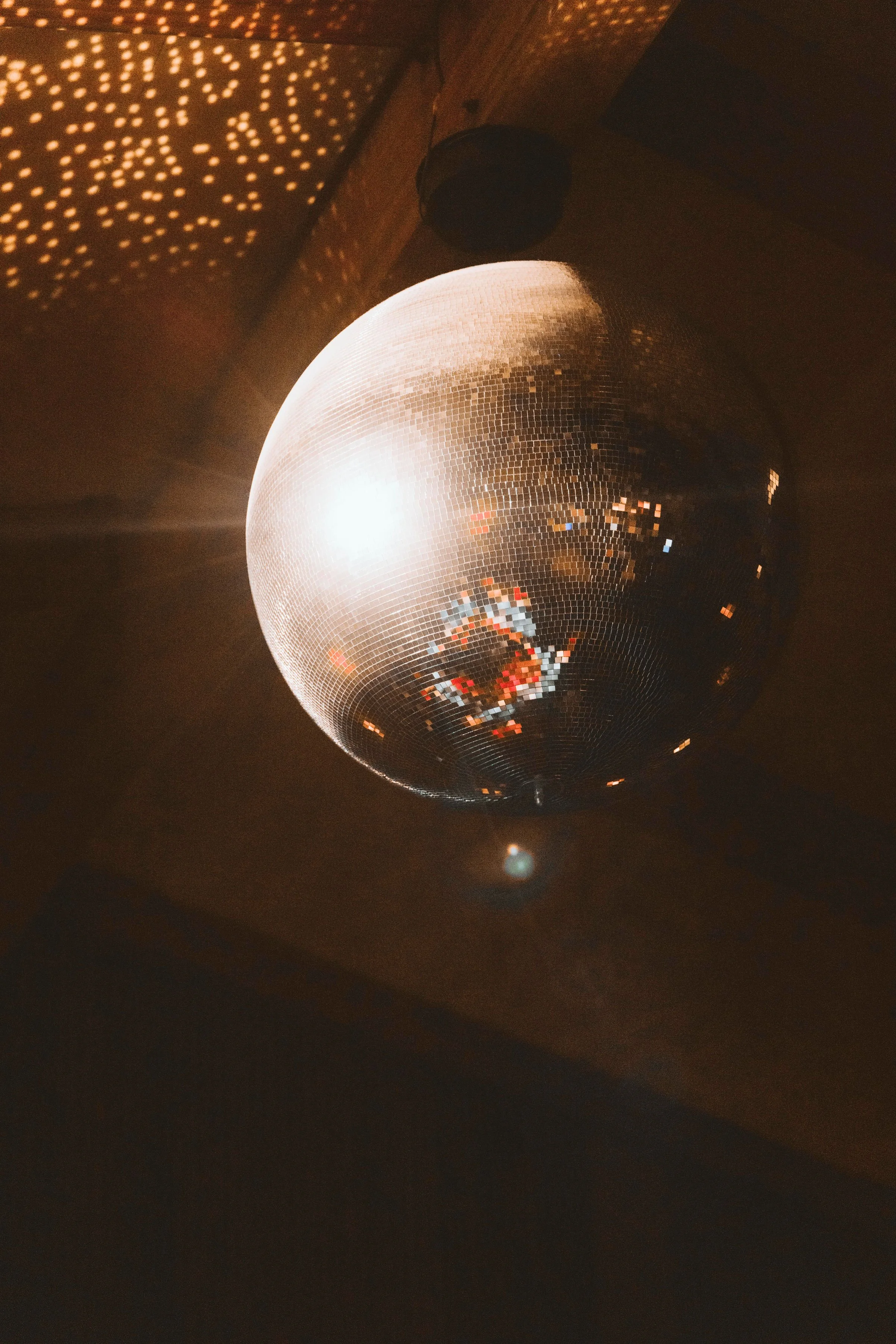 A disco ball hanging from the ceiling, reflecting light and creating patterns on the wall in a dimly lit room at Casa de Afro by Dr. ADO in Mexico City.