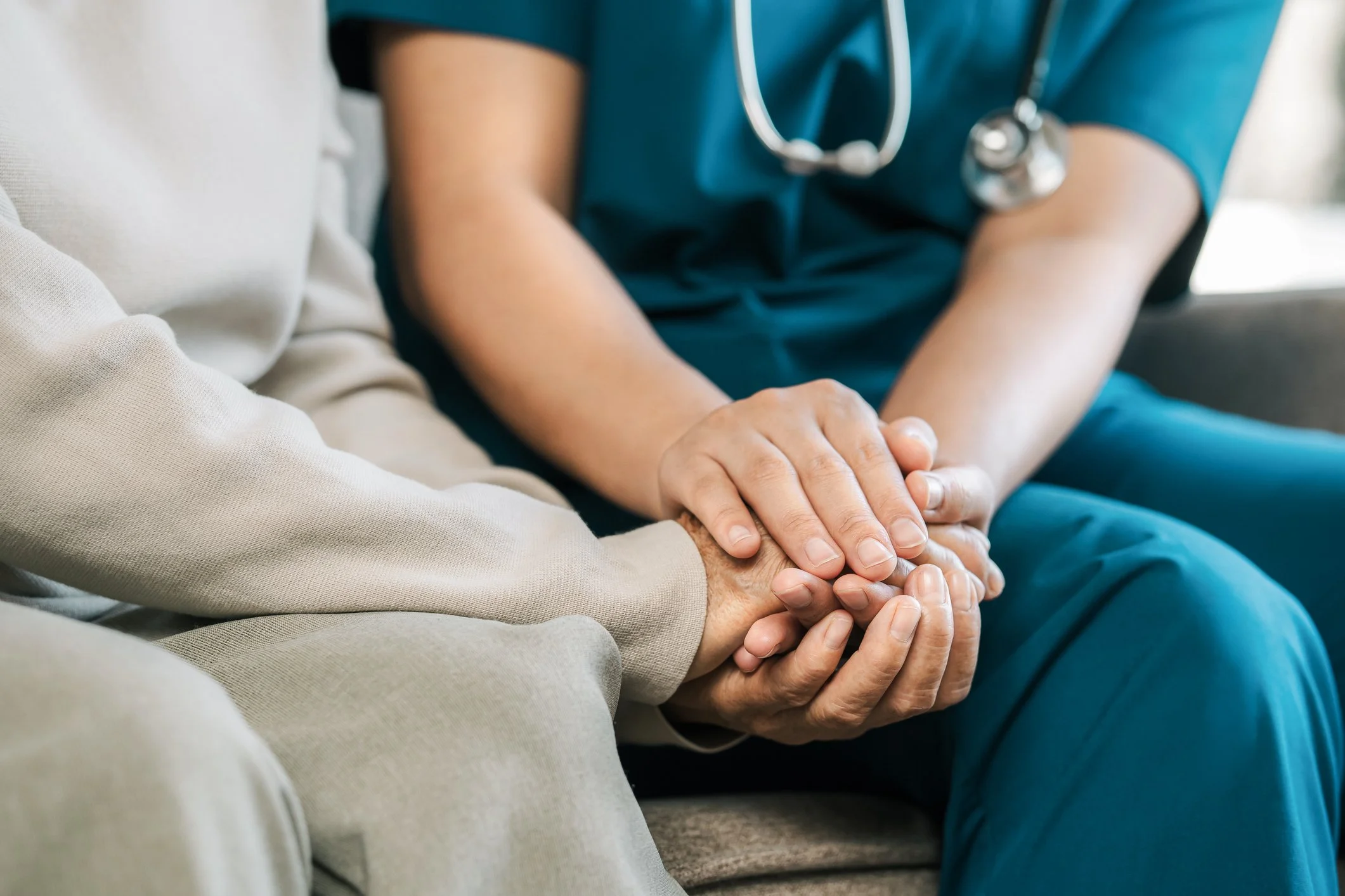A healthcare professional in scrubs holding the hand of a patient in a seated medical setting.