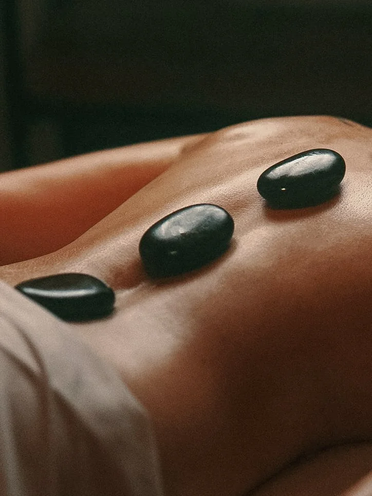 Close-up of black hot stones placed on a person's bare back during a massage therapy session.