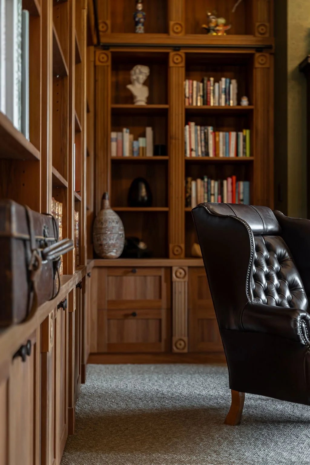 A cozy home library with wooden bookshelves filled with books, a large decorative vase, and a leather armchair.