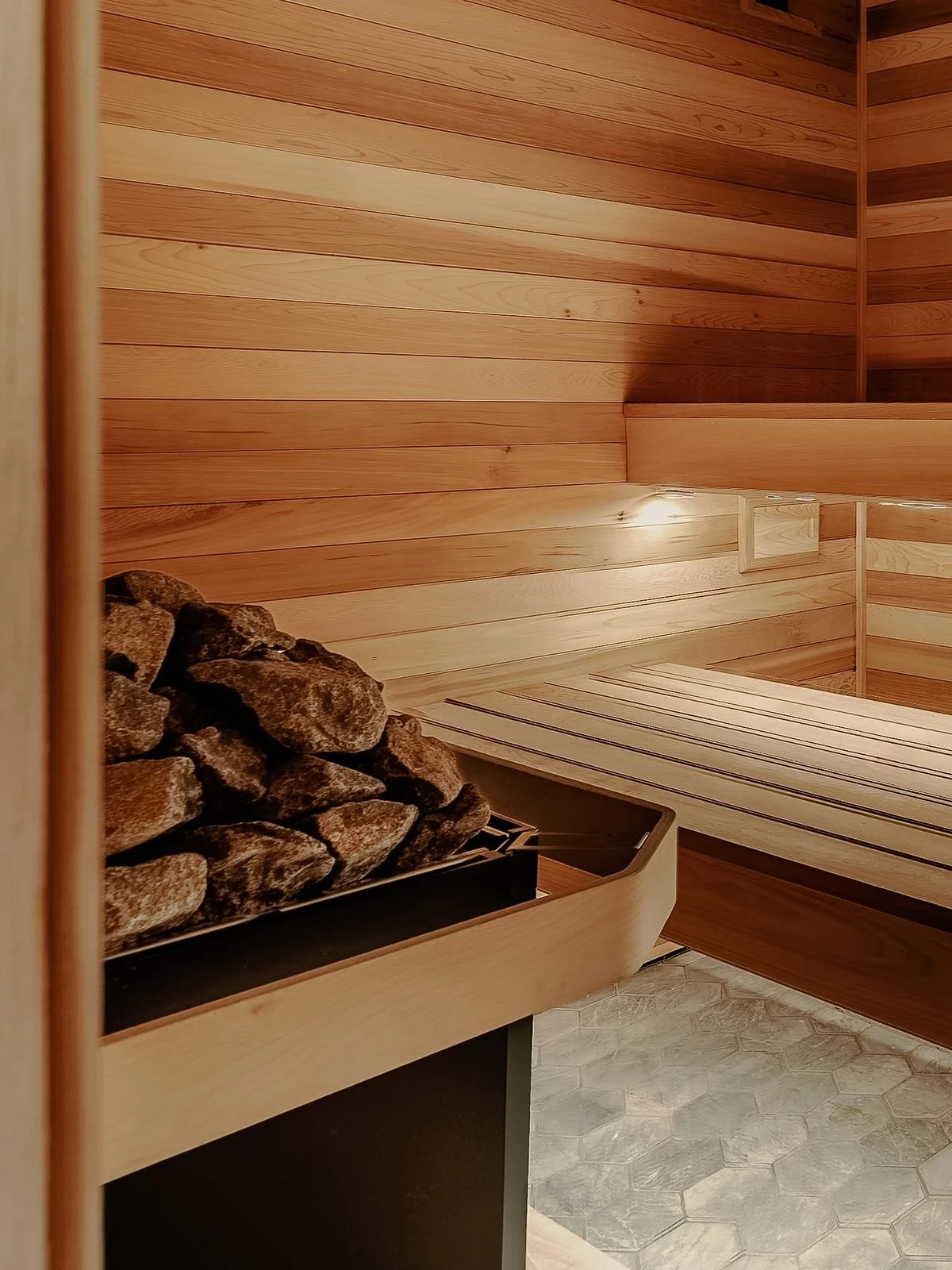 Interior of a wooden sauna with a pile of rocks in a metal container, wooden benches, and warm lighting.
