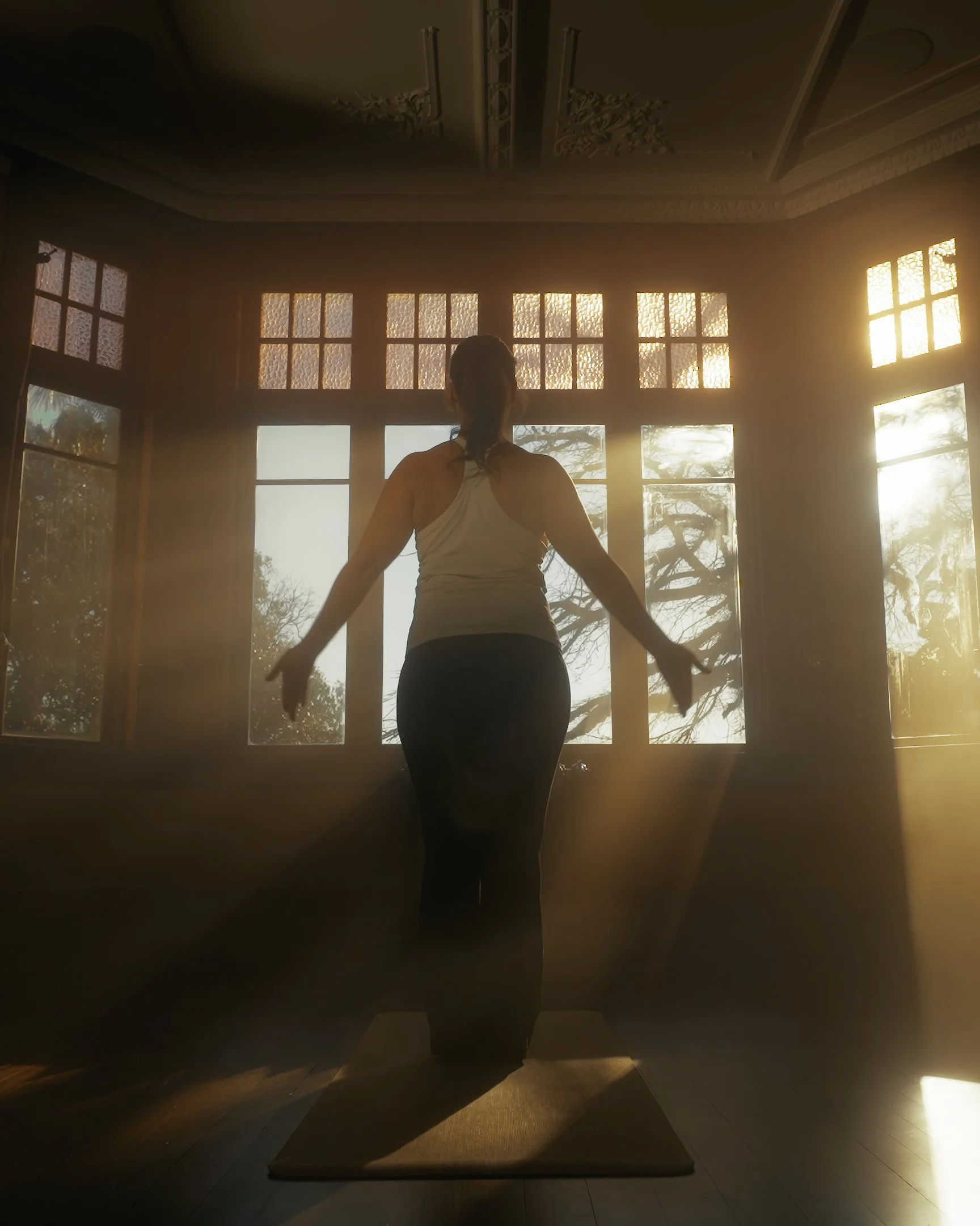 Person practicing yoga or meditation on a mat in front of a large window with sunlight shining through, creating a peaceful atmosphere.