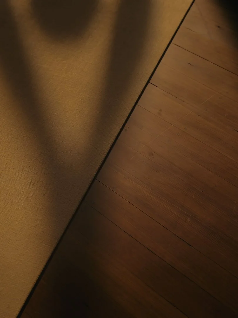 Close-up of a wooden floor next to a textured wall with shadows cast on it.