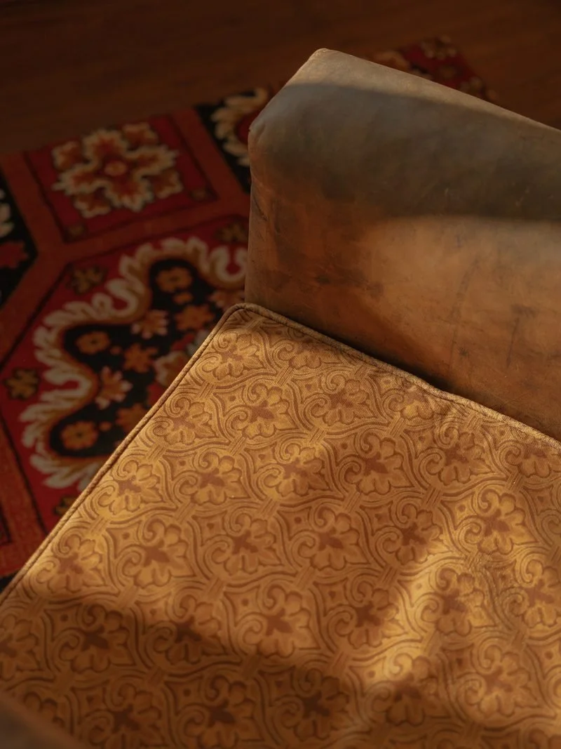 Close-up of a patterned upholstered chair with a wooden backrest, situated on a decorative area rug with floral and geometric motifs.