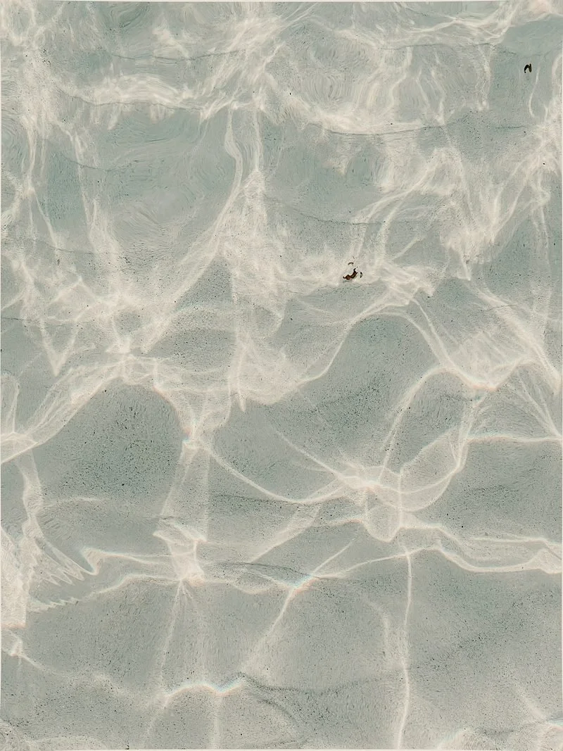 Close-up of shallow clear water with light reflections and tiny rocks or debris at the bottom