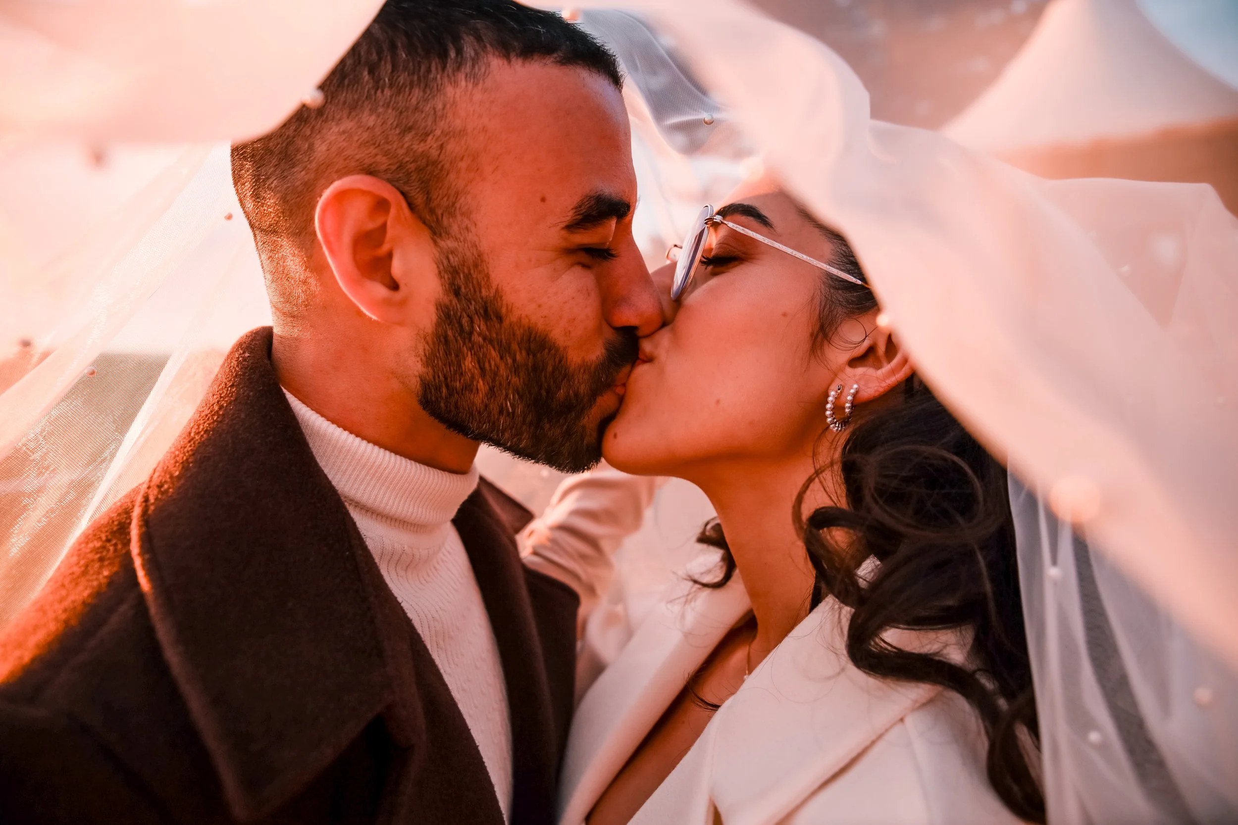 A couple kissing under a white veil during a wedding celebration.
