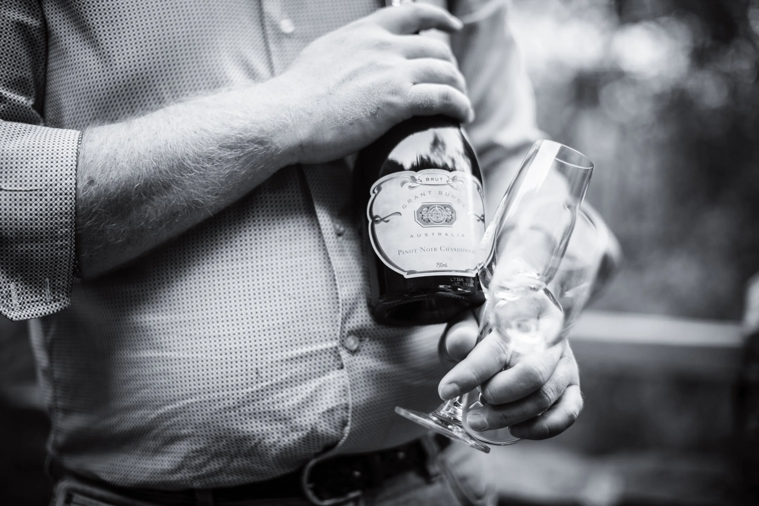 A person holding a bottle of Grant Burge wine and an empty champagne flute