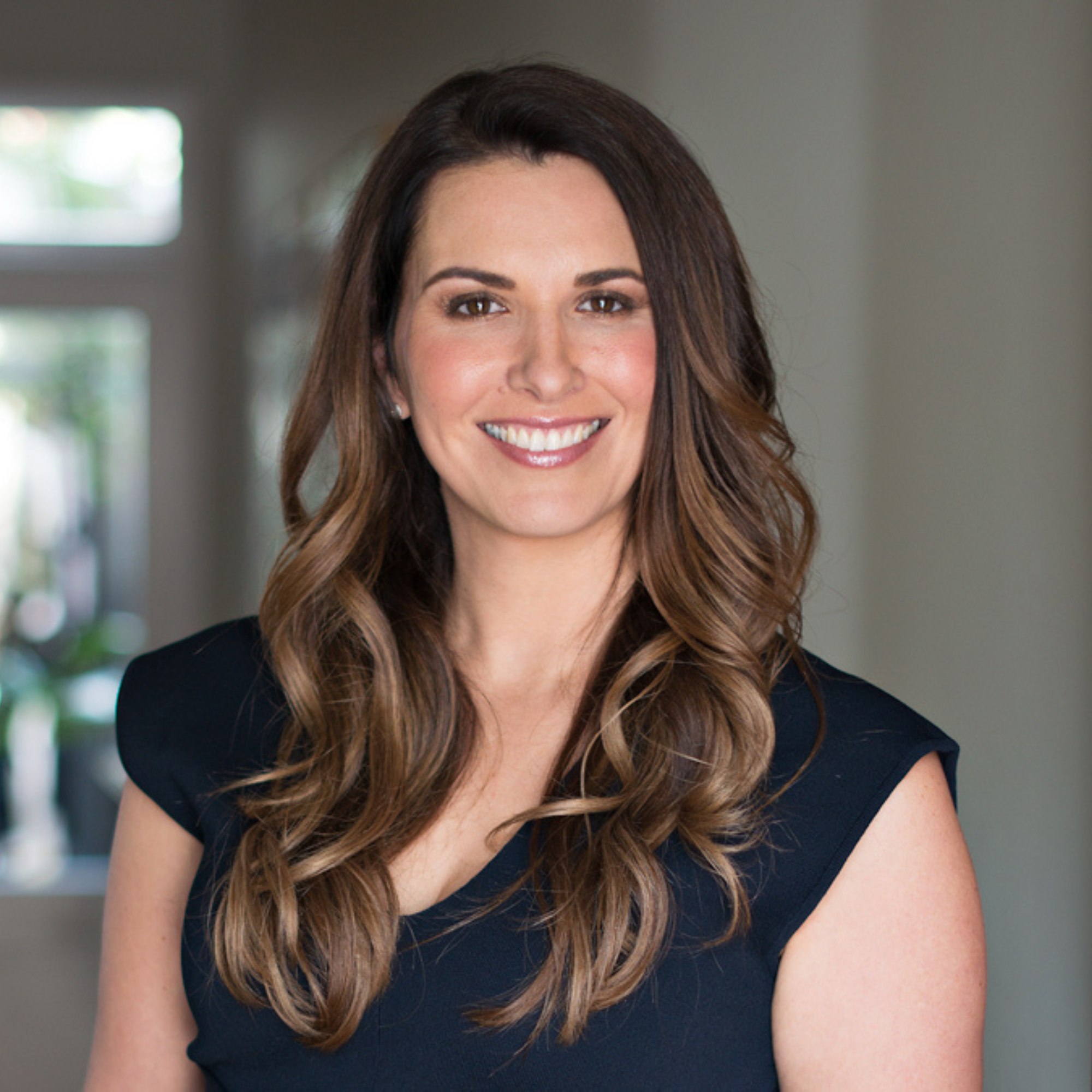A woman with long, wavy brown hair smiling in an indoor setting.