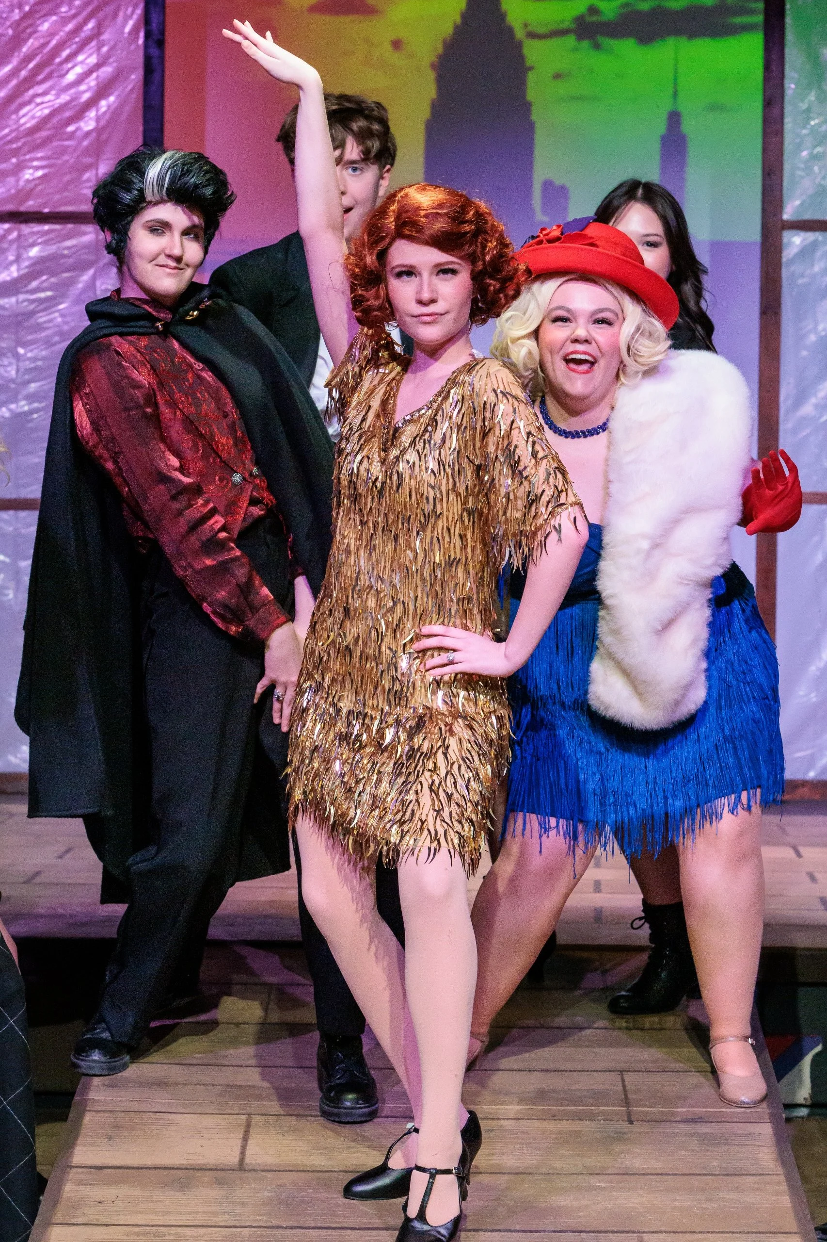 Drowsy Chaperone musical number. Group of five people dressed in colorful costumes, posing on stage with a colorful background and wooden floor.