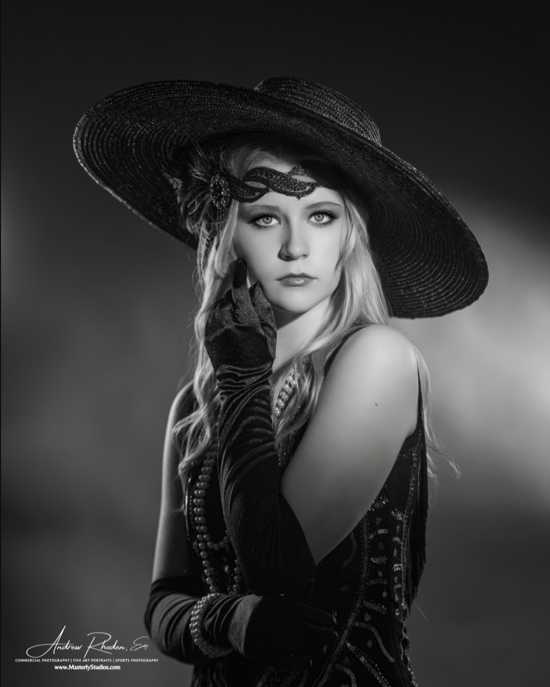 Addison Skyler model in 20s shoot. A woman with fair skin and long, wavy hair dressed in vintage style, wearing a large wide-brimmed hat, long gloves, and jewelry, posing with her hand near her chin in a black-and-white portrait.