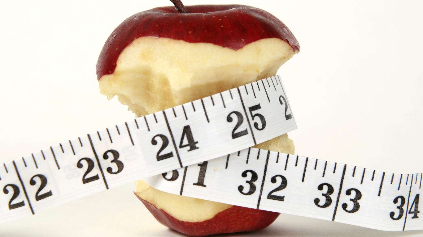 Half-eaten red apple with a measuring tape wrapped around it, showing measurements from approximately 22 to 33 centimeters.